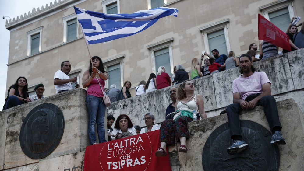 An anti-austerity protester waves a Greek flag above a banner which reads: "The other Europe with Tsipras" during a rally in front of the parliament in Athens, Greece [AP]