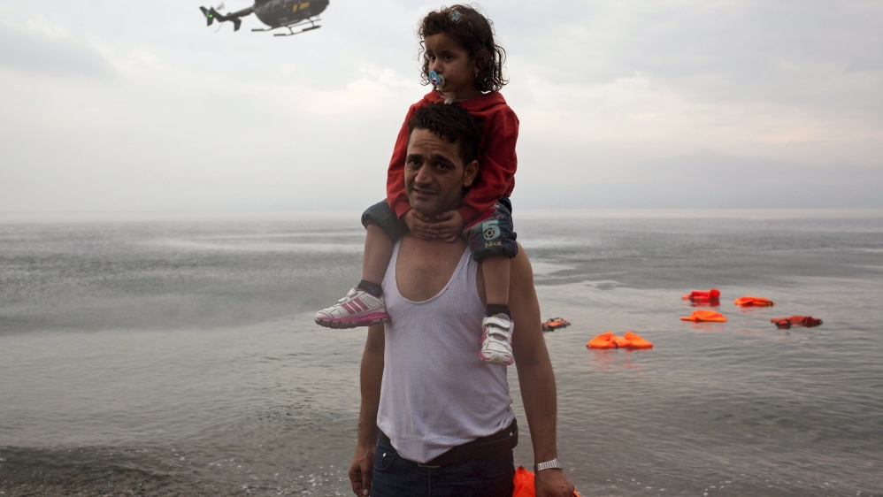 A Syrian refugee carries his daughter as a Frontex helicopter flies over on the Greek island of Lesbos