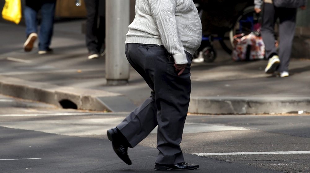 A man crosses a main road as pedestrians carrying food walk along the footpath in central Sydney, Australia