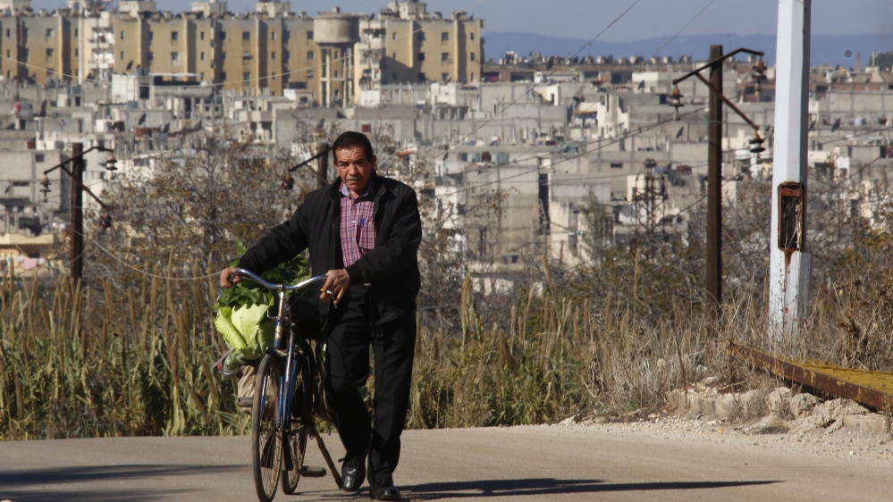A man is seen pushing his bicycle in an area adjacent to the Waer neighborhood in the central city of Homs, Syria [AP]