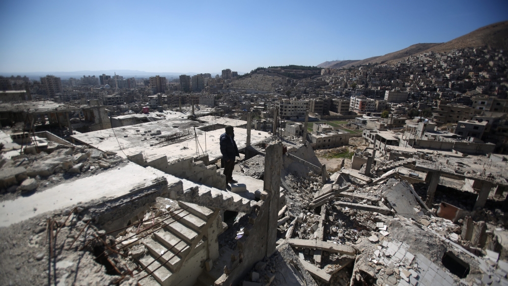A Syrian man stands on top of a damaged building in Barzeh neighborhood of Damascus, Syria [EPA]