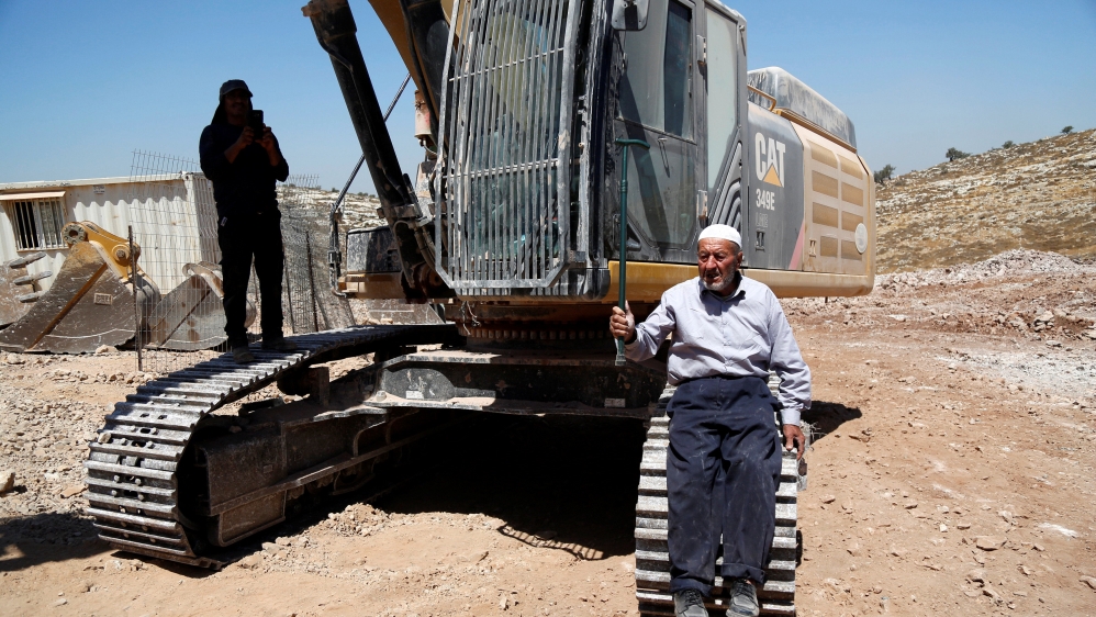 A Palestinian man sits on a tracks of an Israeli excavator as he tries to prevent it from clearing his land during a protest against Jewish settlements, near the West Bank city of Ramallah [REUTERS]