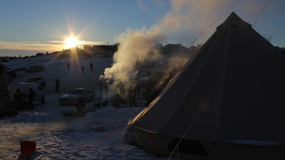 
The sun drops behind Facebook Hill. Wood stoves burn outside, before being moved into teepees and tents to provide heat [Adam Levinson/Al Jazeera] 
