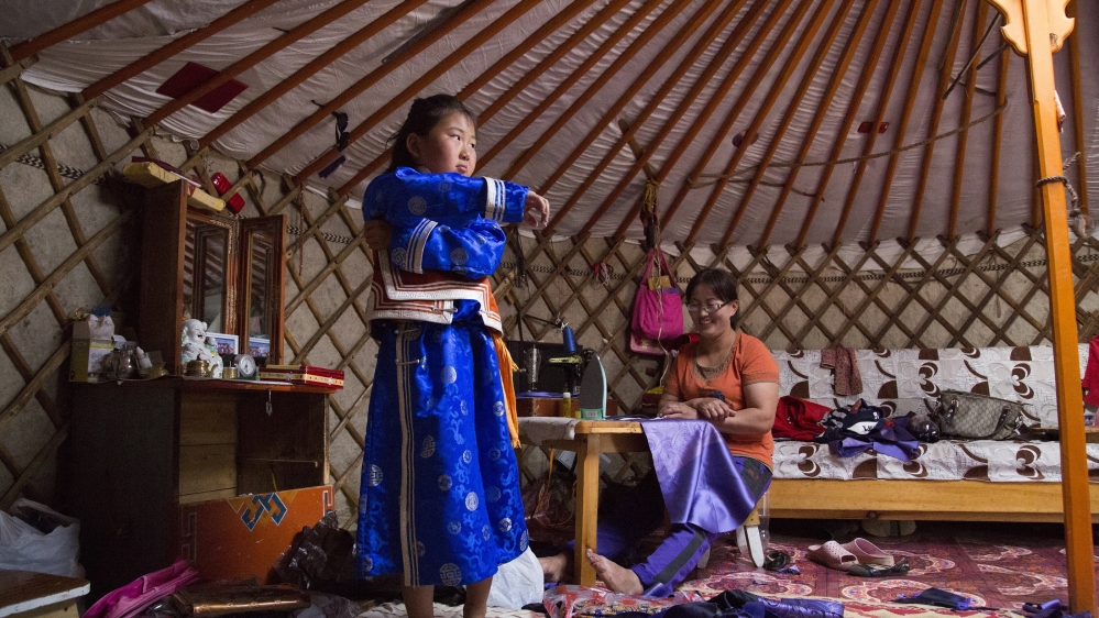 Bujinlkham tries on a deel her mother, Muukhtsetseg, left, has sewn for her to wear during the Naadam festival [Hannah Griffin/Al Jazeera]