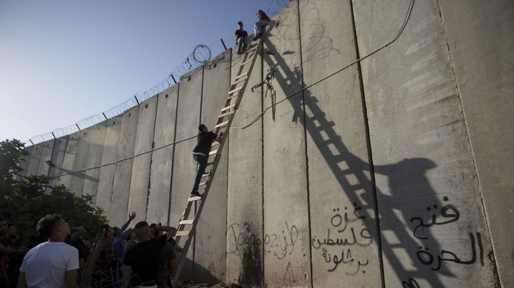 Palestinians use a ladder to climb over the separation barrier with Israel on their way to pray at the Al-Aqsa Mosque in Jerusalem, on the Friday of the Muslim holy month of Ramadan, in Al-Ram, north