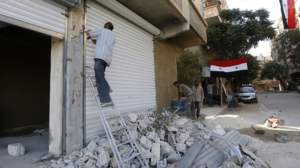 Syrian flags hang from buildings as workers rebuild destroyed stores in Harasta, on the outskirt of the Syrian capital Damascus on July 15, 2018.