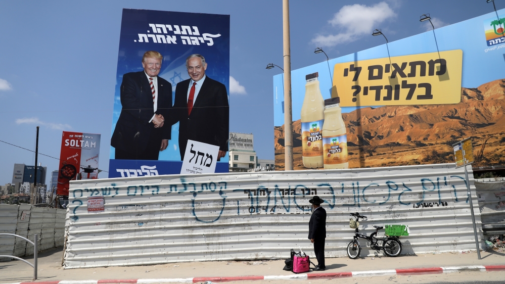 An ultra-Orthodox Jewish man stands next to a Likud party election campaign banner depicting Israeli Prime Minister Benjamin Netanyahu and U.S. President Donald Trump in Bnei Brak, Israel