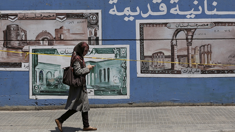 A woman walks by a wall painted with images of Lebanon''s old currency along a street of the Arab University in Beirut August 10, 2012