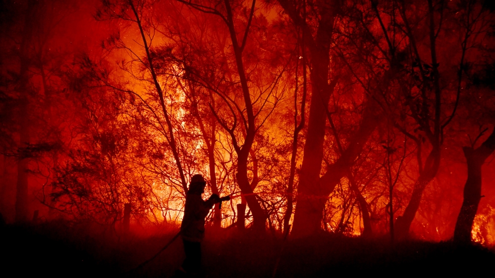 Rural Fire Service (RFS), NSW Fire and Rescue, National Parks and Wildlife Service (NPWS) officers and local residents fight a bushfire encroaching on properties near Kioloa, Australia