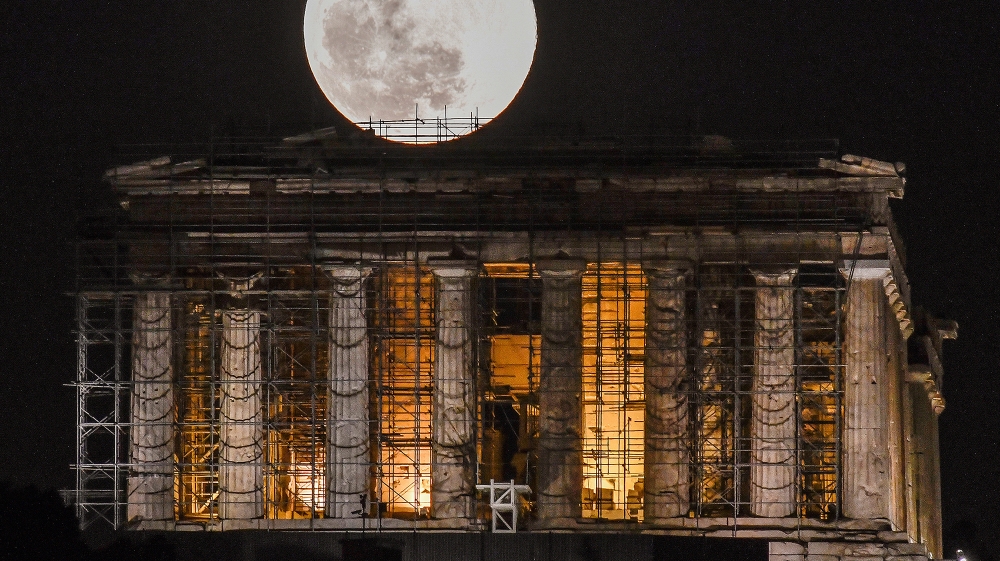 A full moon rises above Greek Parthenon Temple (438 BC), covered by scaffolding, at the Acropolis archaeological site in Athens on February 9, 2020 . LOUISA GOULIAMAKI / AFP