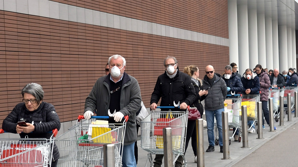 epaselect epa08289489 People wearing protective face masks lined up at a safe distance in front of a supermarket in Milan, Italy, 12 Mrch 2020. Tougher lockdown measures kicked-in in Italy on the day