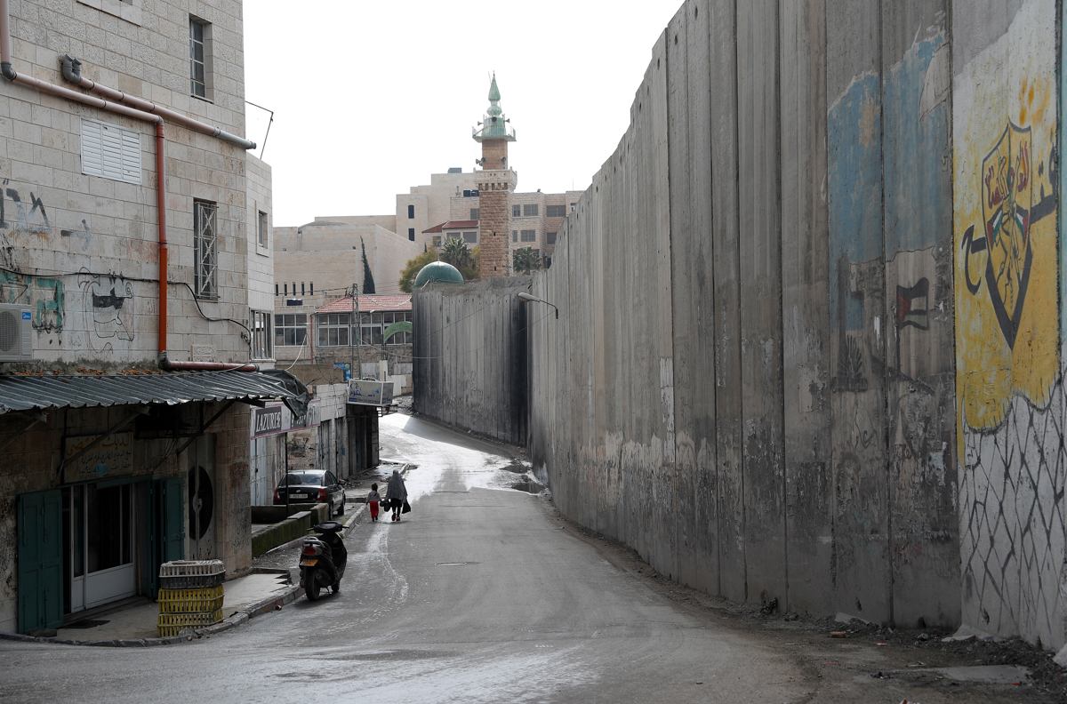A woman and a child walk along the wall separating East Jerusalem from the Palestinian village of Abu Dis, the proposed Palestinian capital in US President Donald Trump plan for the Middle east, on Ja
