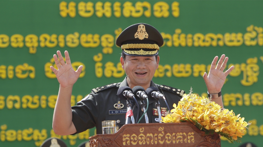 Hun Manet speaks at a podium with arms raised.
