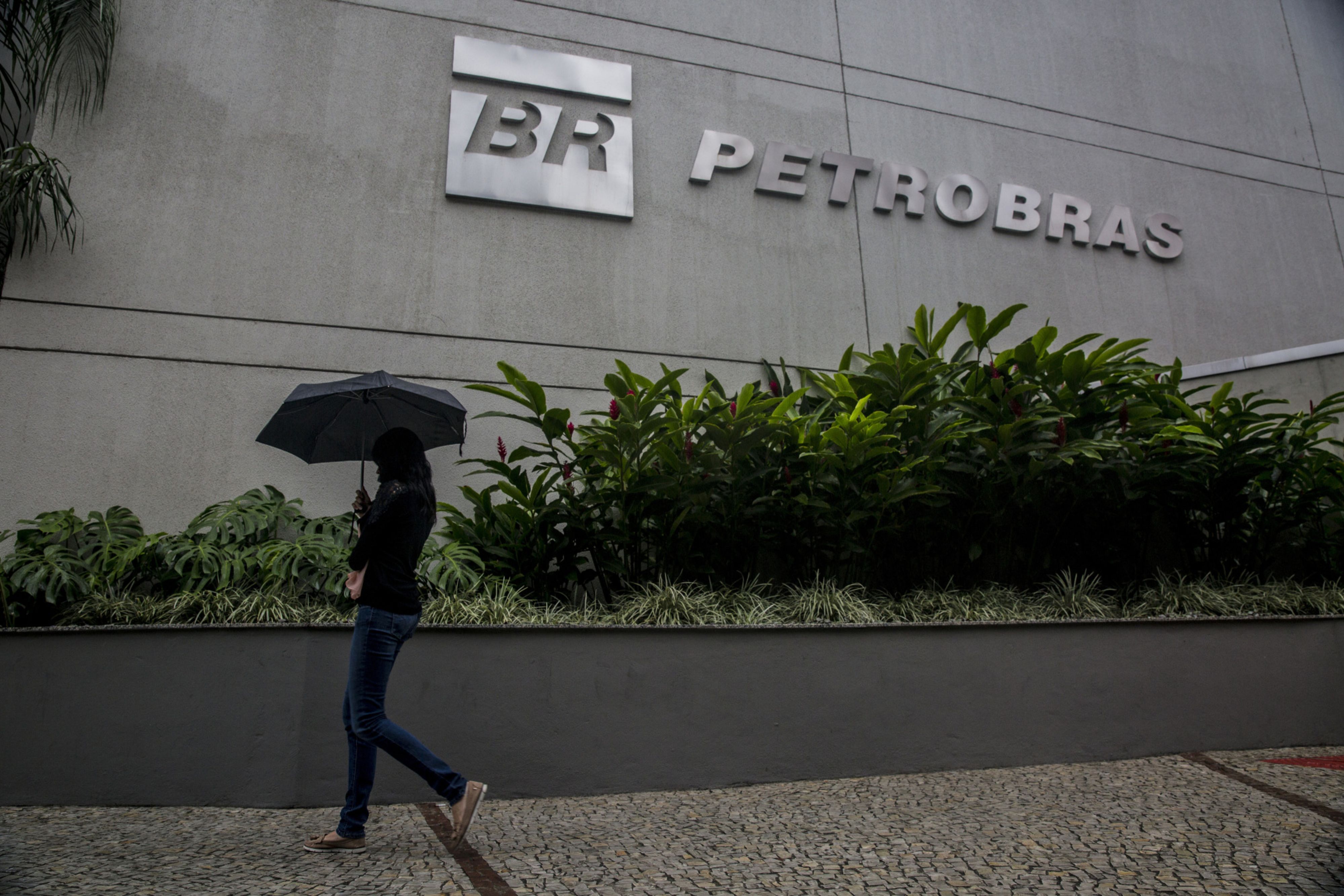 A pedestrian with an umbrella walks past the Petrobras headquarters in Rio de Janeiro, Brazil.