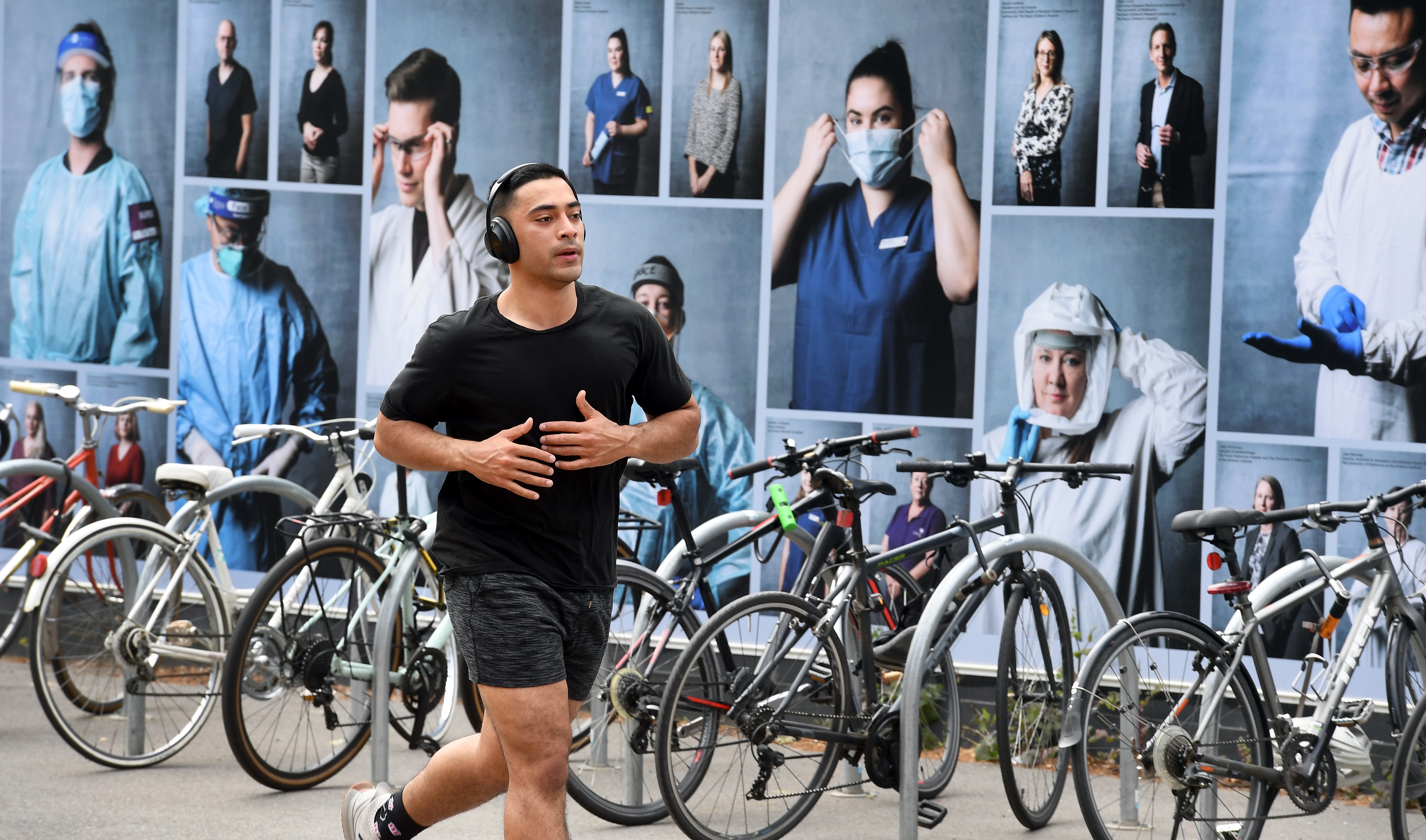 A man jogs past a display of photos or front-line medical workers outside the Royal Melbourne Hospital on October 20, 2020 [William West/ AFP]