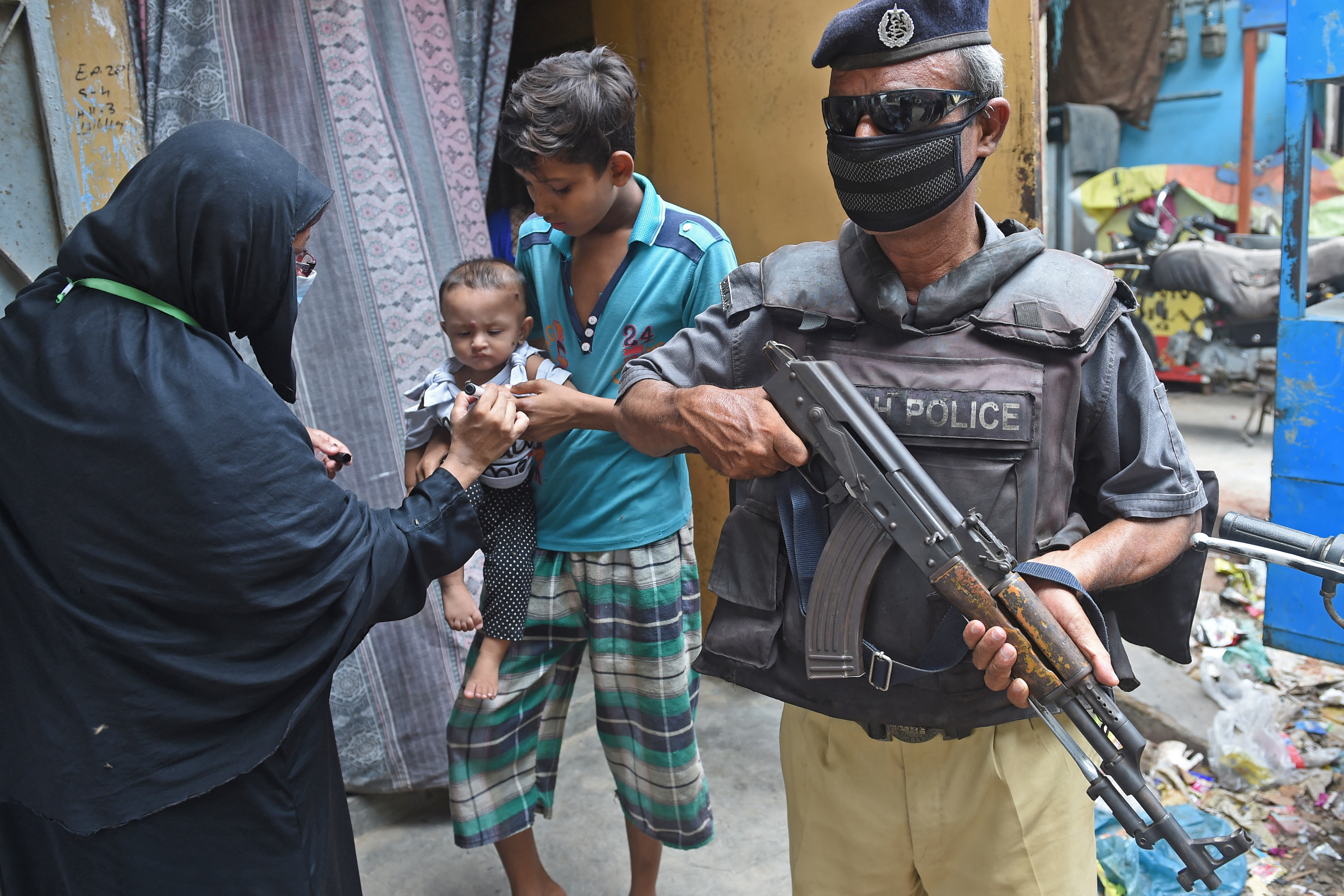 A policeman stands guard as a health worker marks the finger of a child after administering polio vaccine drops in Karachi [File: Rizwan Tabassum/AFP]