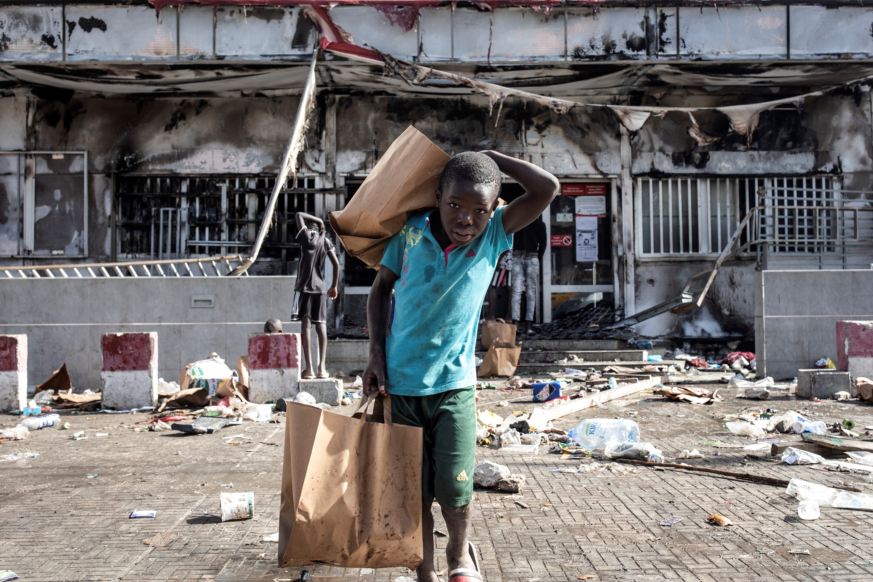A young boy holds grocery bags as he walks away from a burned down and looted Auchan supermarket in the upmarket area of Almadies in Dakar on Saturday [John Wessels/AFP]