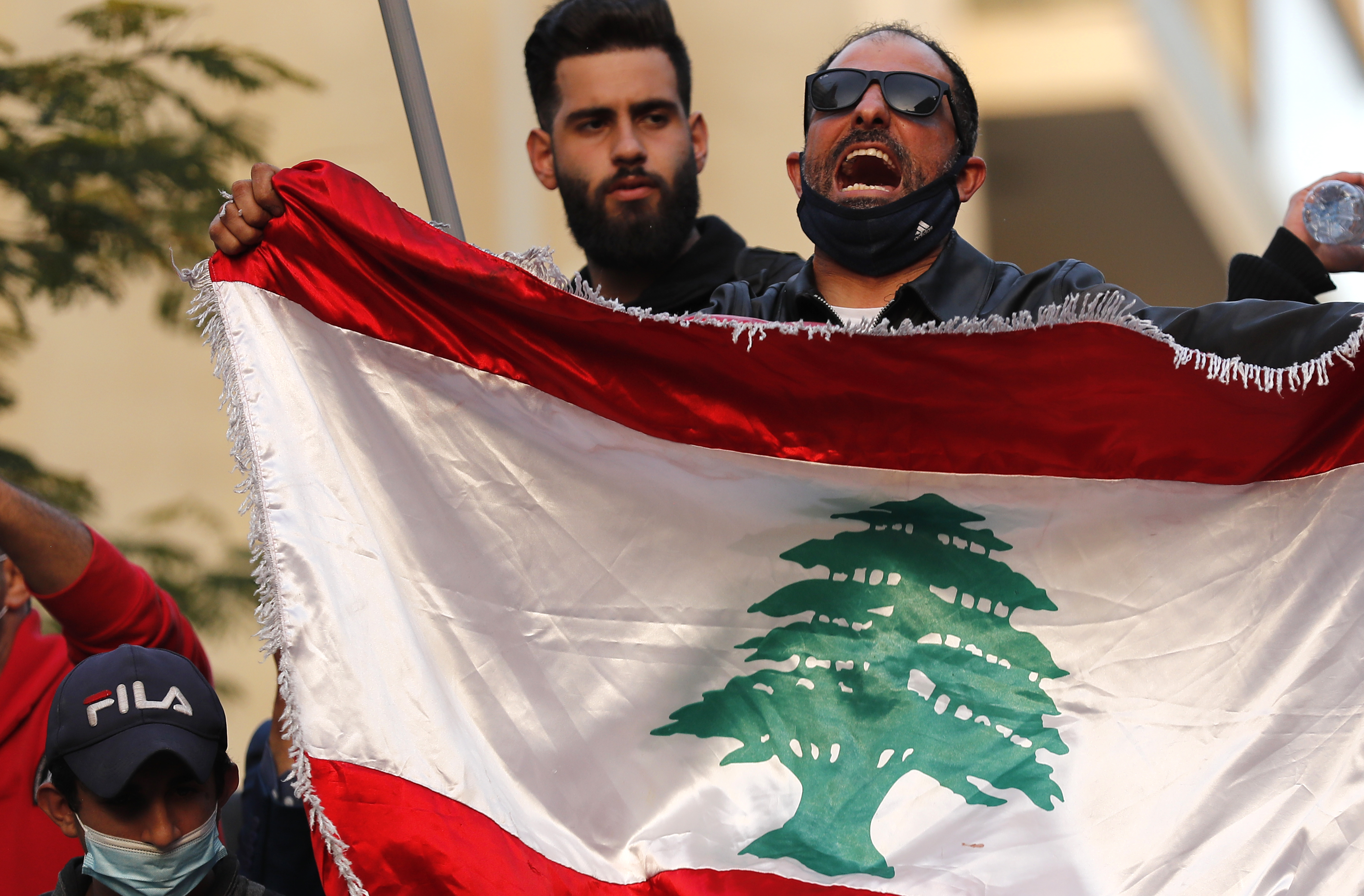 A protester holds the national flag during demonstrations demanding local banks allow people to withdraw their money [Hussein Malla/AP]