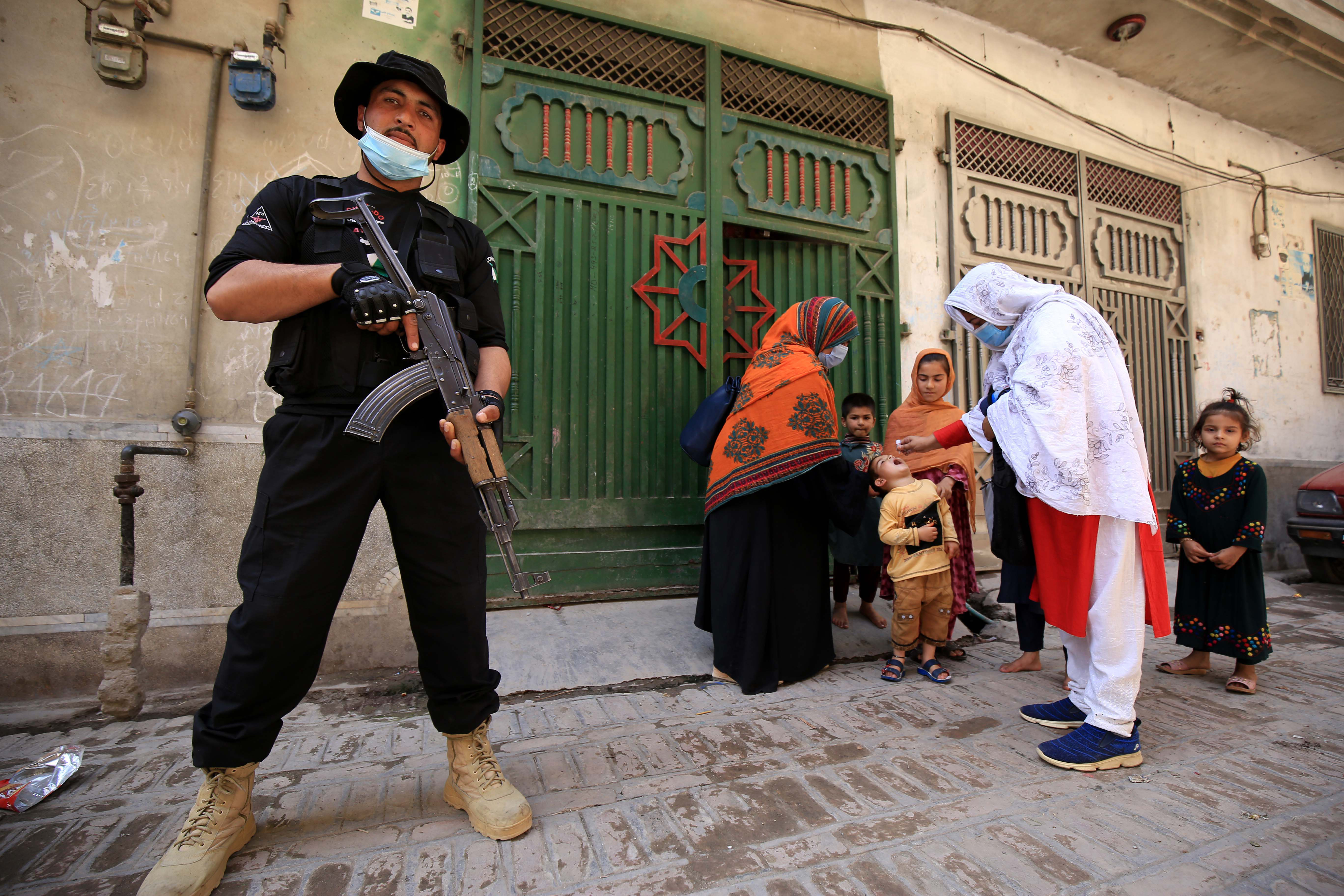 A police officer stands guard as health workers administer polio vaccine to children during a door-to-door vaccination campaign, as the spread of COVID-19 continues, in Peshawar, Pakistan [File: Bilawal Arbab/ EPA]