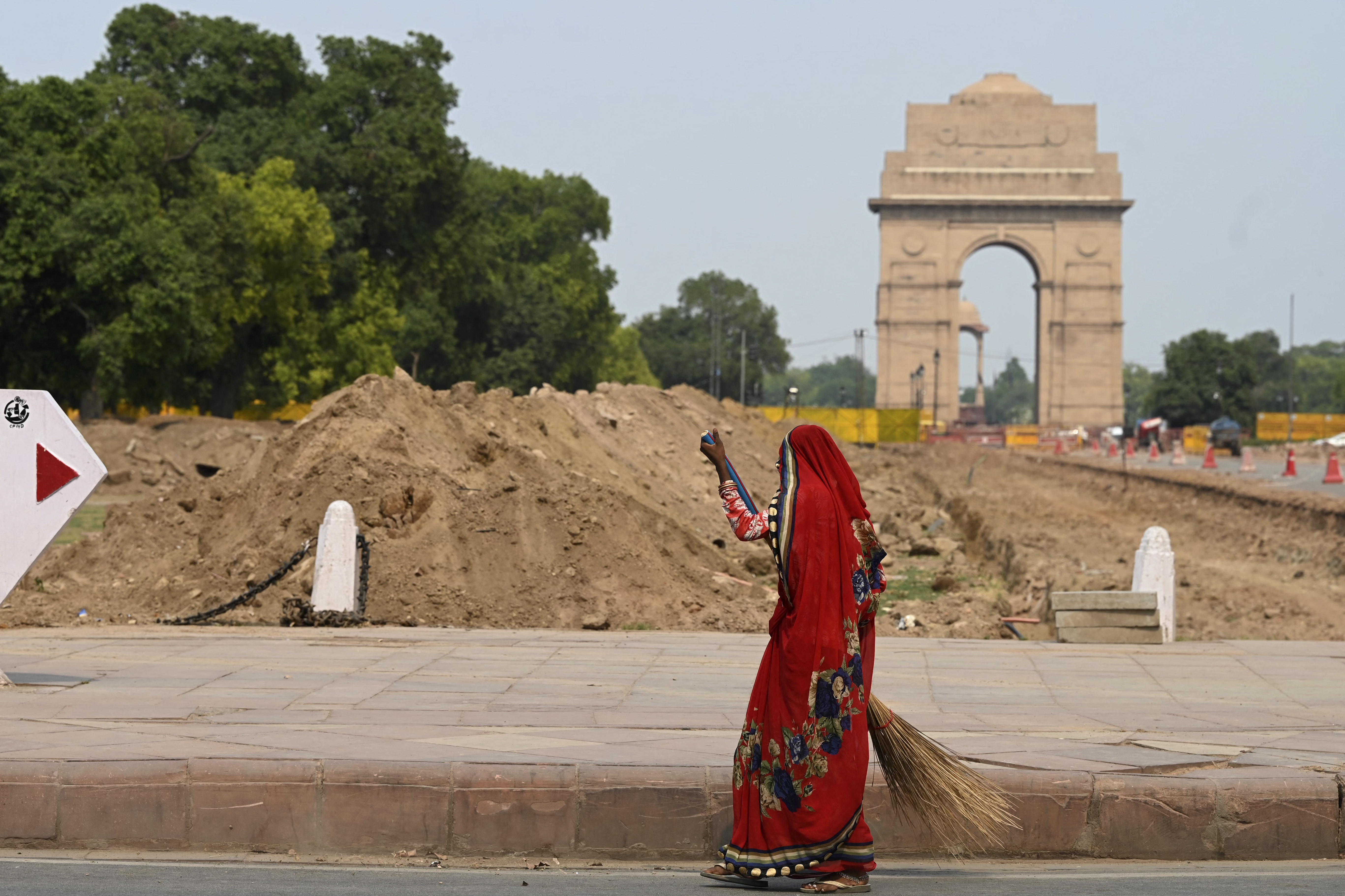 A woman sweeps next to the redevelopment site of the Central Vista project along the Rajpath road in New Delhi [Sajjad Hussain/AFP]