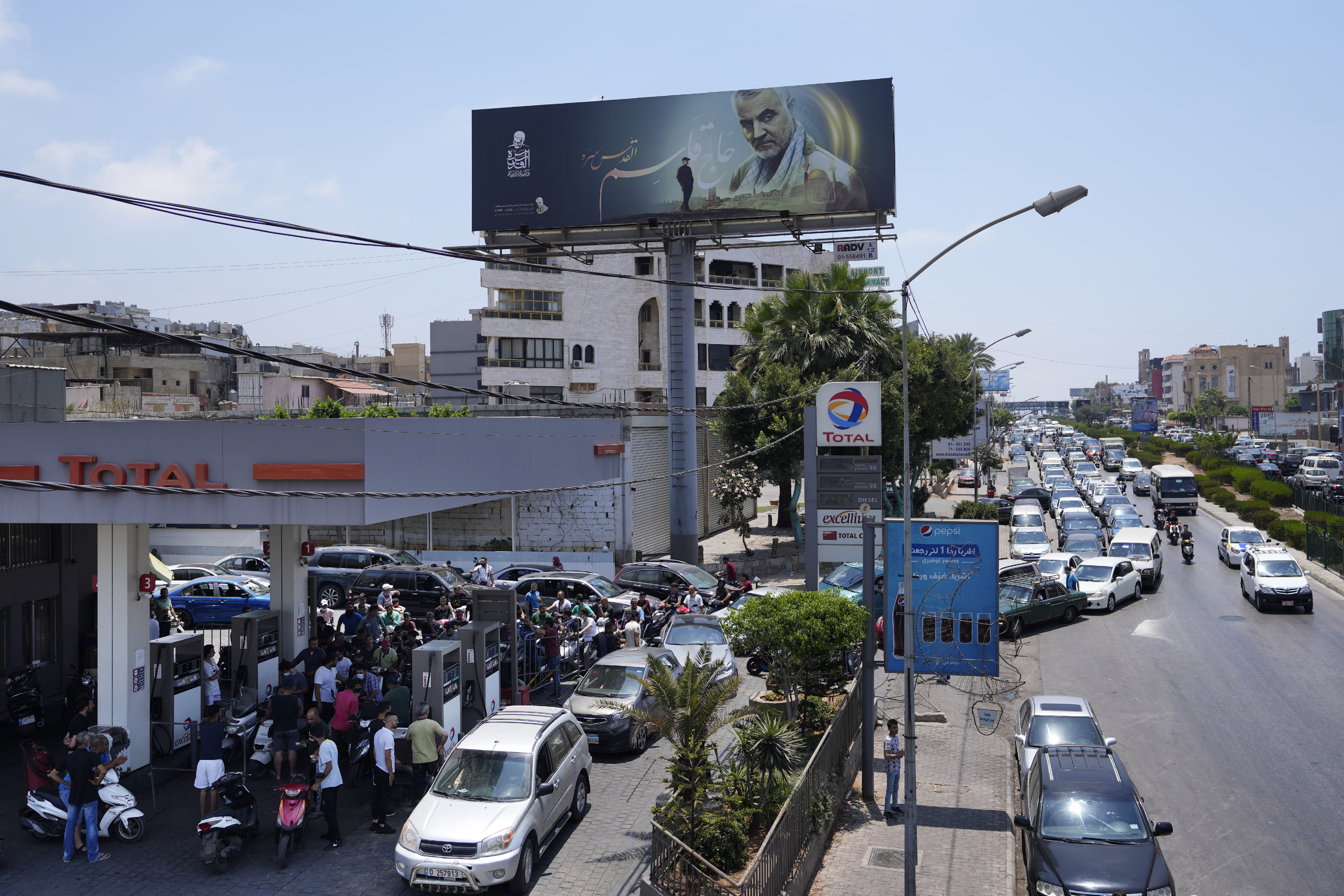Drivers wait in a long queue to get fuel at a petrol station under a billboard showing slain IRGC General Qassem Soleimani [File: Hassan Ammar/AP Photo]