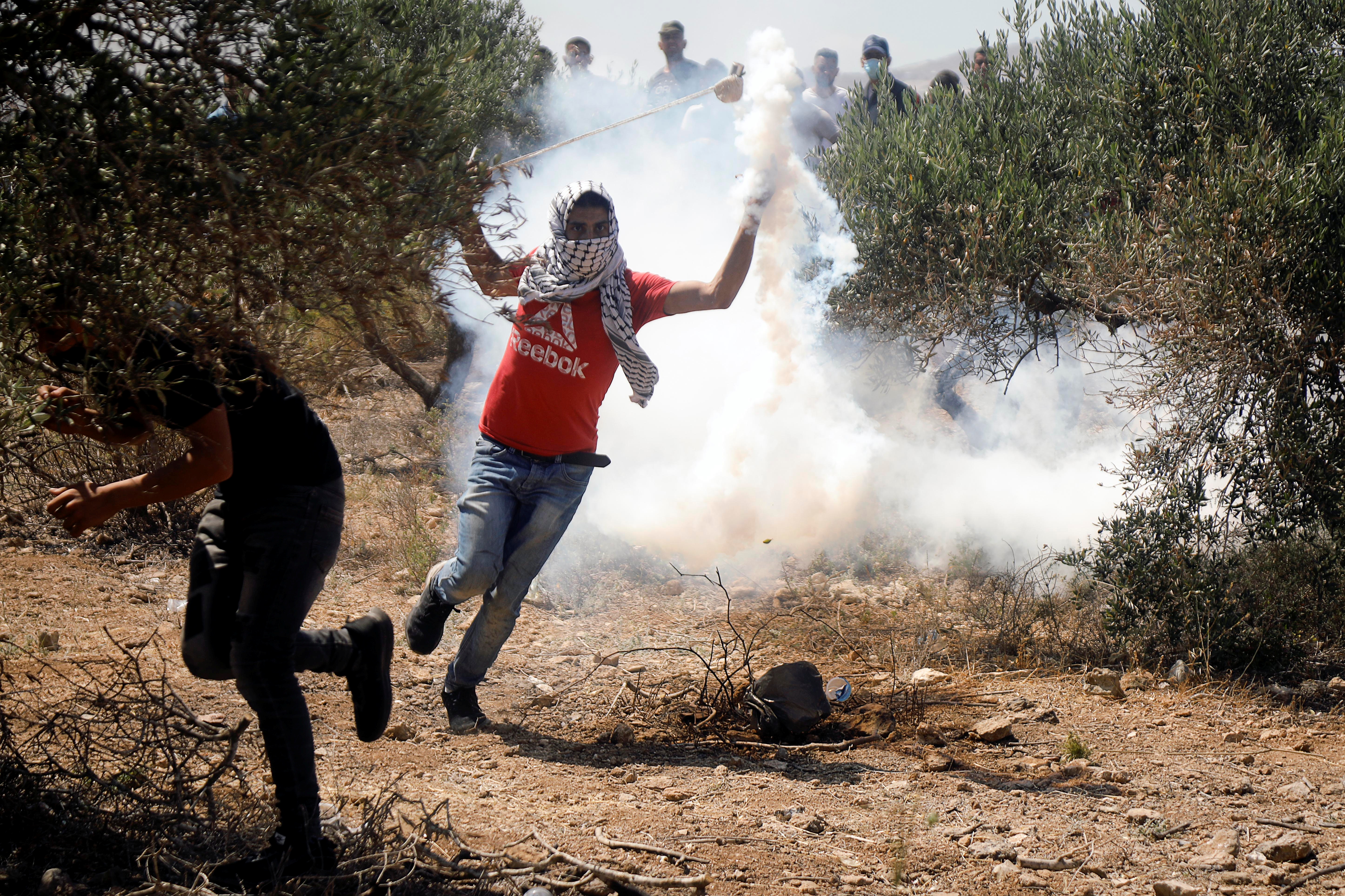 A Palestinian demonstrator throws back a tear gas canister fired by Israeli forces during a protest against Israeli settlements in Beita in the Israeli-occupied West Bank [Raneen Sawafta/Reuters]