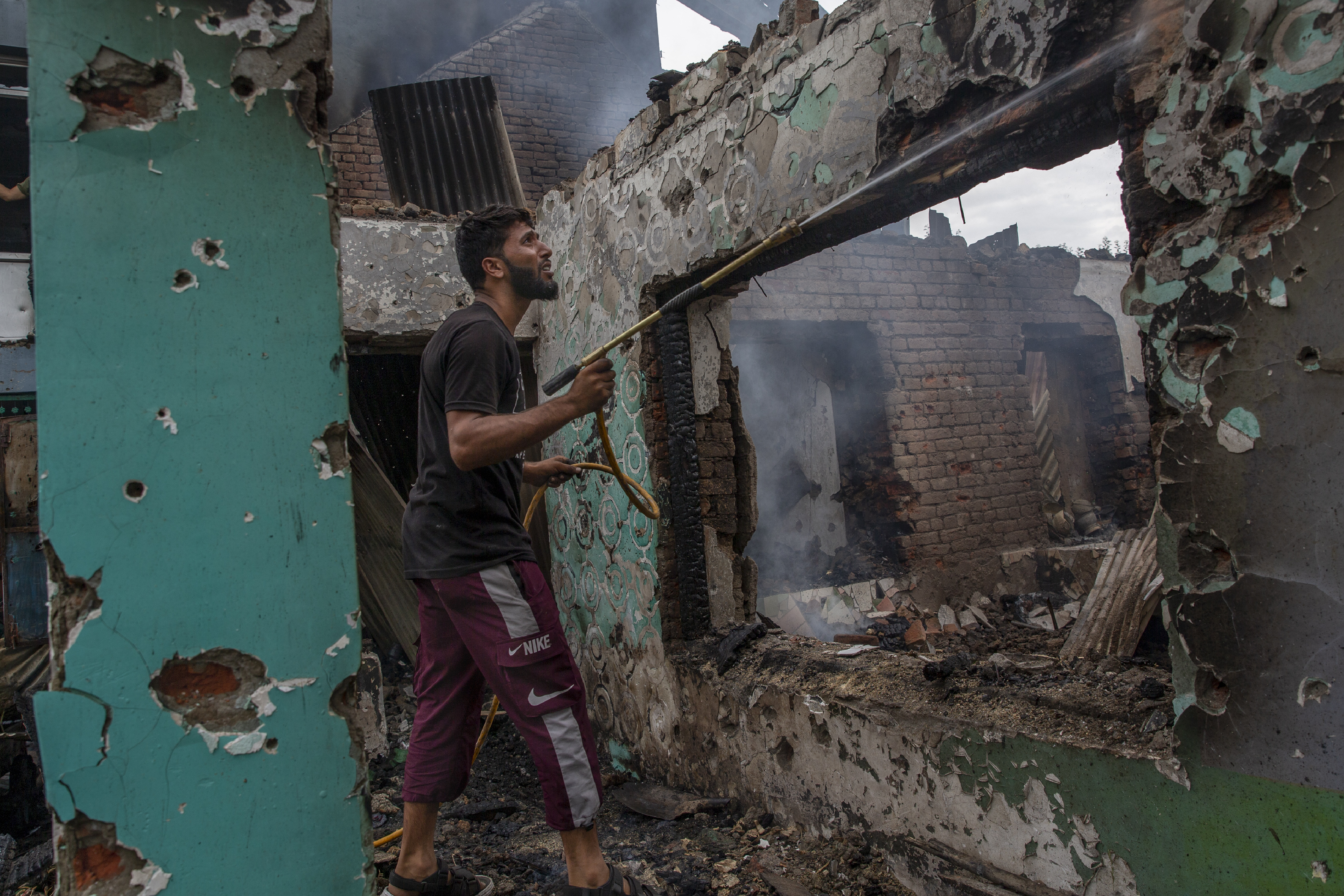 A Kashmiri villager sprays water on burning debris as he clears a house destroyed in a gunfight in Pulwama, south of Srinagar. [Dar Yasin/AP Photo]