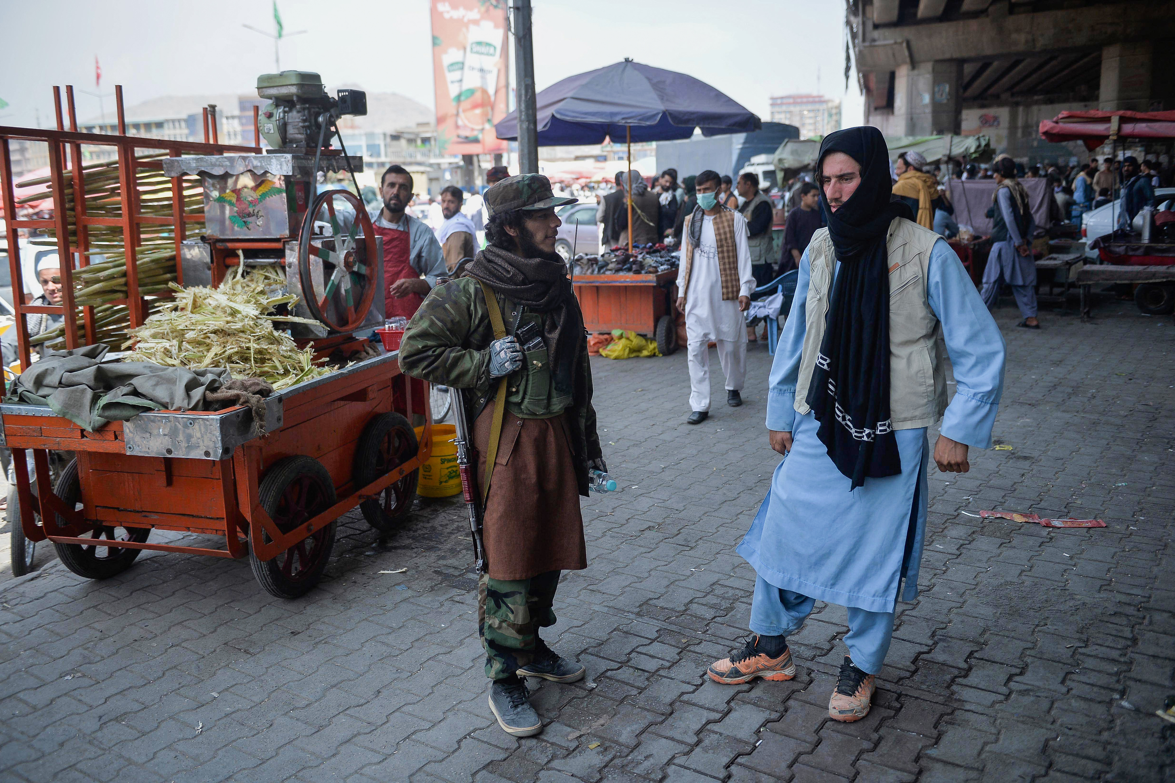 A Taliban fighter stands by a kiosk selling sugarcane juice at a market area, flocked with local Afghan people at Kote Sangi area of Kabul on August 17, 2021, after Taliban seized control of the capital following the collapse of the Afghan government. (Photo by Hoshang Hashimi / AFP) (AFP)