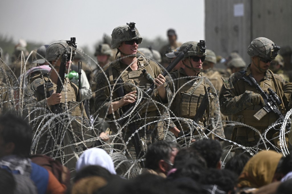 US soldiers stand guard as Afghans sit on a roadside near the military part of the airport in Kabul [Wakil Kohsar/AFP]