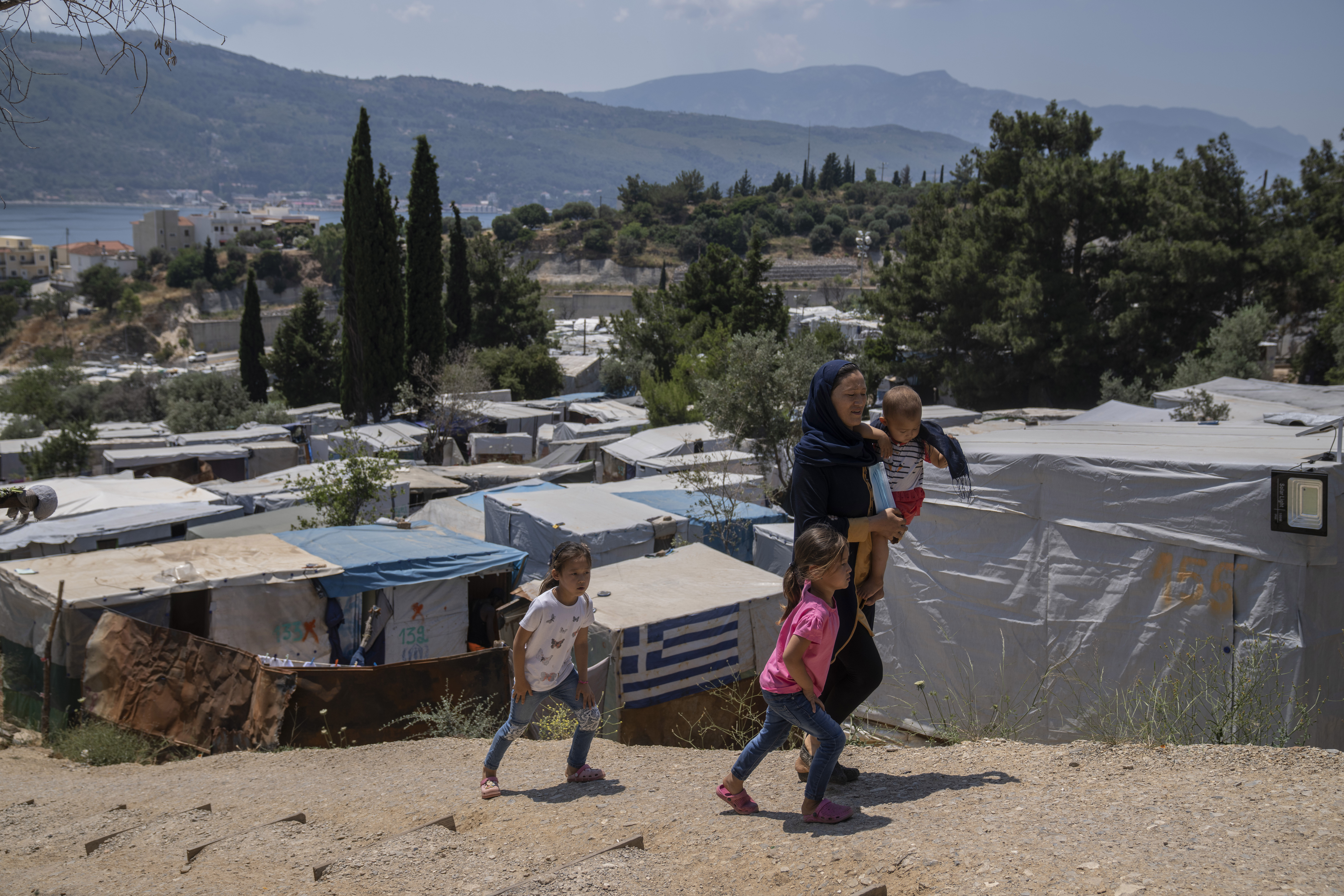 An Afghan woman with her three children walk outside the perimeter of a Greek refugee camp [File: Petros Giannakouris/AP Photo]