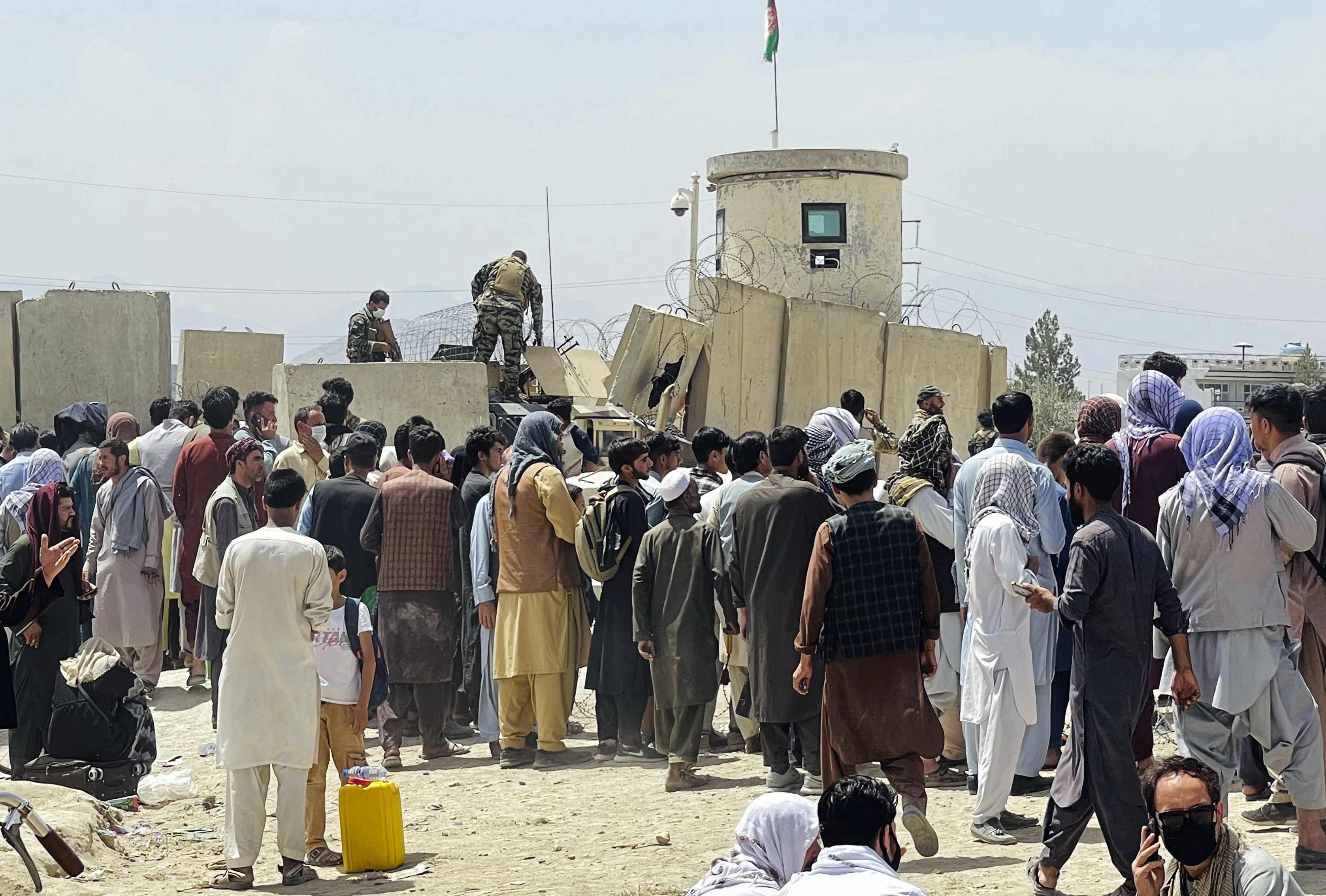Afghan security guards stand on a wall as hundreds of people gather outside the international airport in Kabul, Afghanistan [AP Photo]