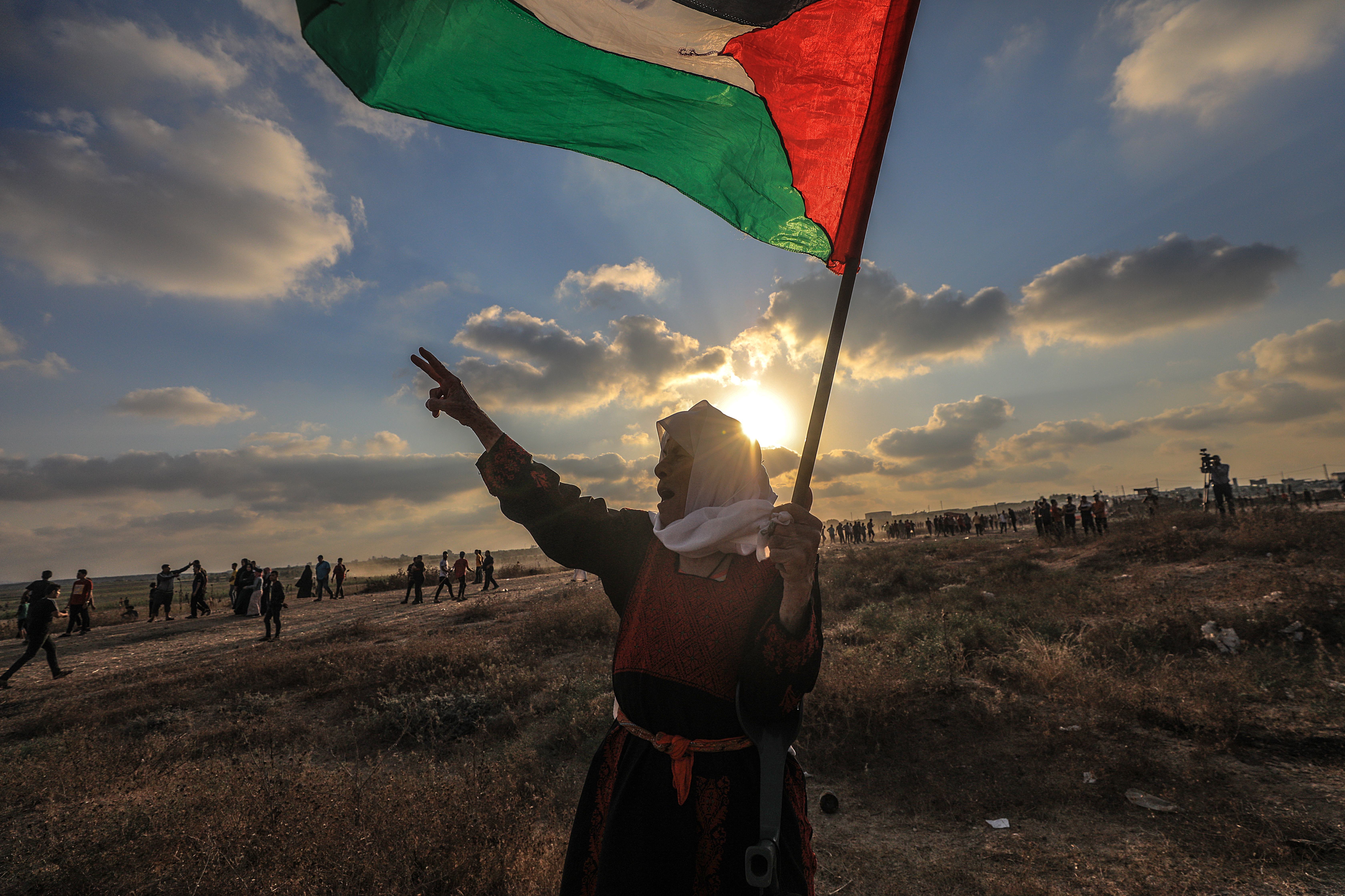 An elderly Palestinian woman holds a Palestinian flag during the protests near the boundary between Israel and the Gaza Strip. [Mohammed Saber/EPA]