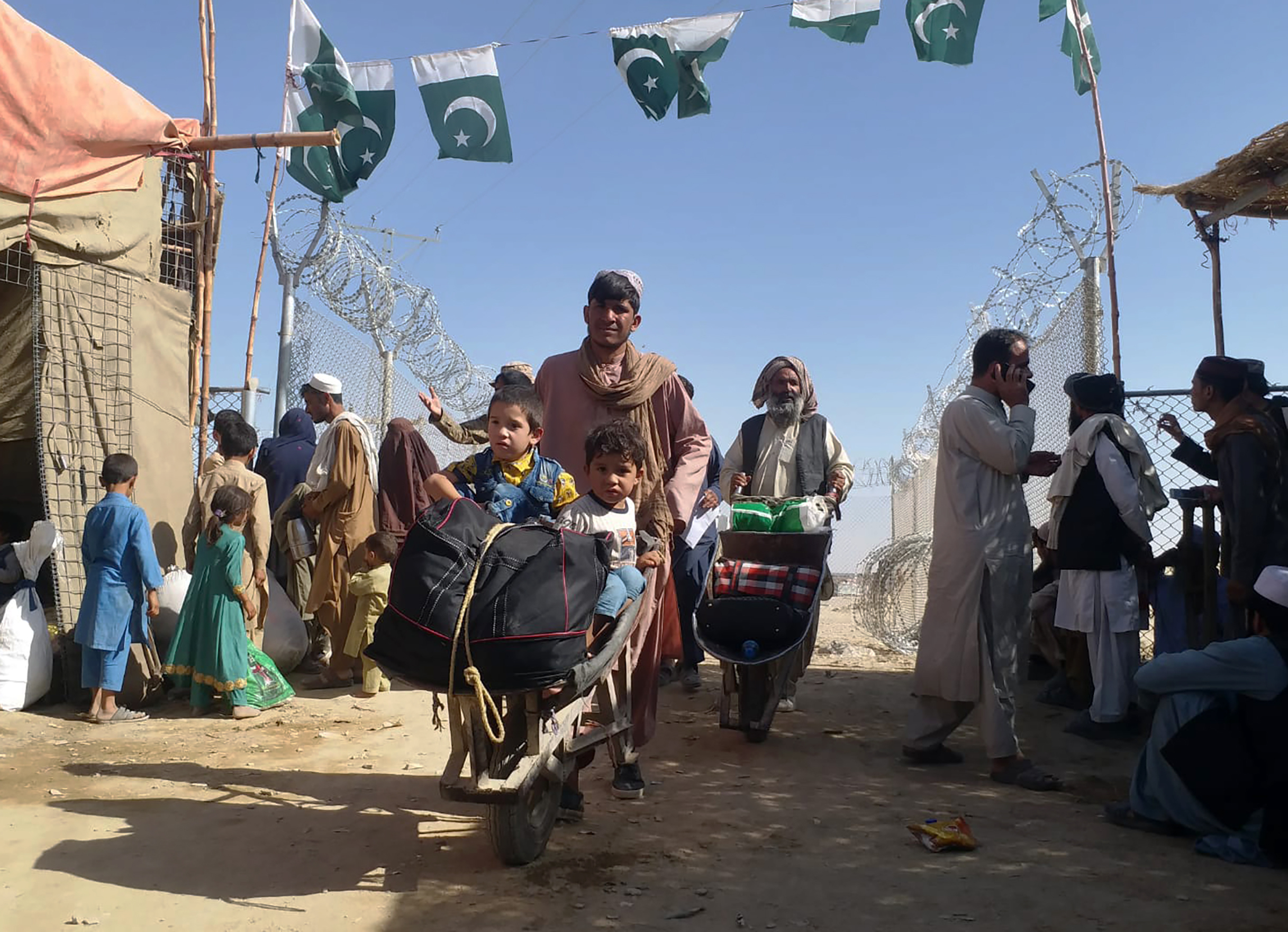 A porter pushes a wheelbarrow carrying children as Afghan refugees enter Pakistan through a border crossing point in Chaman, Pakistan [Jafar Khan/AP]