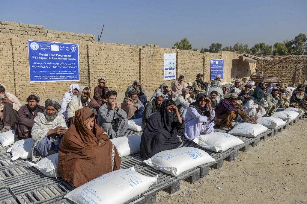 Afghan people sit besides sacks of food aid distributed by the WFP in Kandahar [File: Javed Tanveer/AFP]