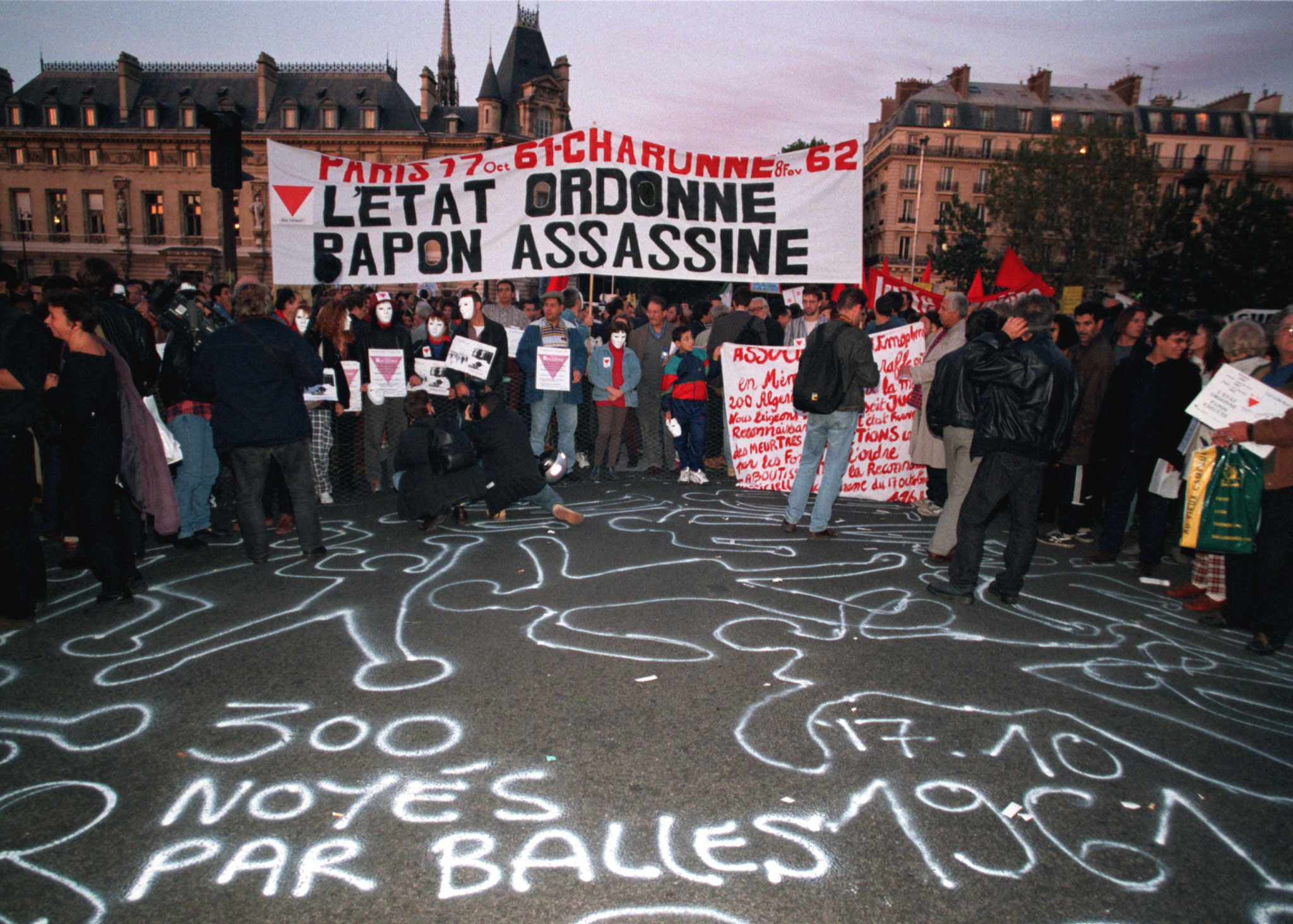 At a 1997 protest, people hold a banner reading &#39;The State Orders - Papon Assassinates&#39; in front of an inscription on the pavement, &#39;300 drowned by bullets&#39; [File: Reuters]