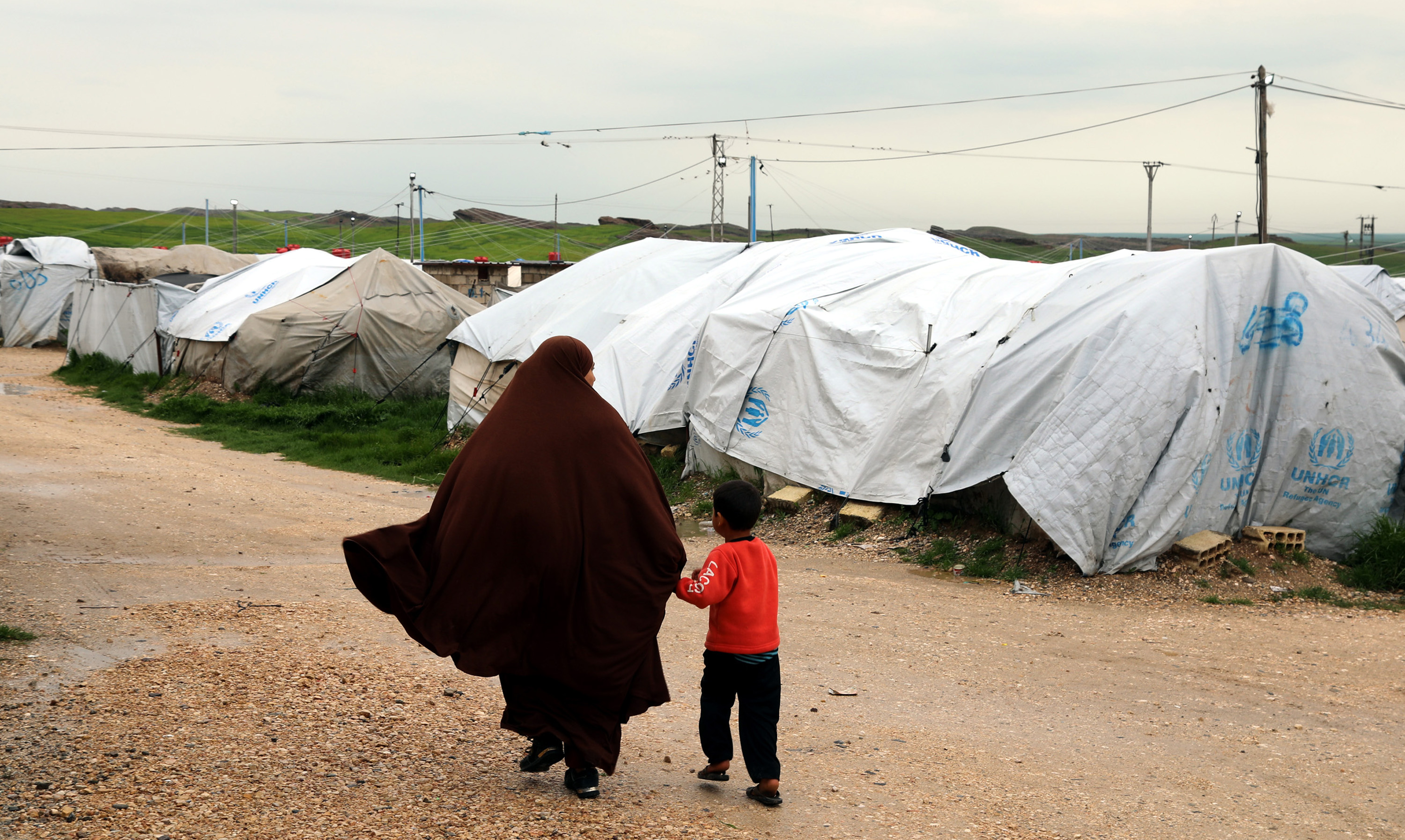 In this file photo from March 2019, a woman, reportedly a wife of a suspected ISIL fighter, walks with her son at Roj refugee camp in northeastern Syria [File: Ahmed Mardnli/EPA]