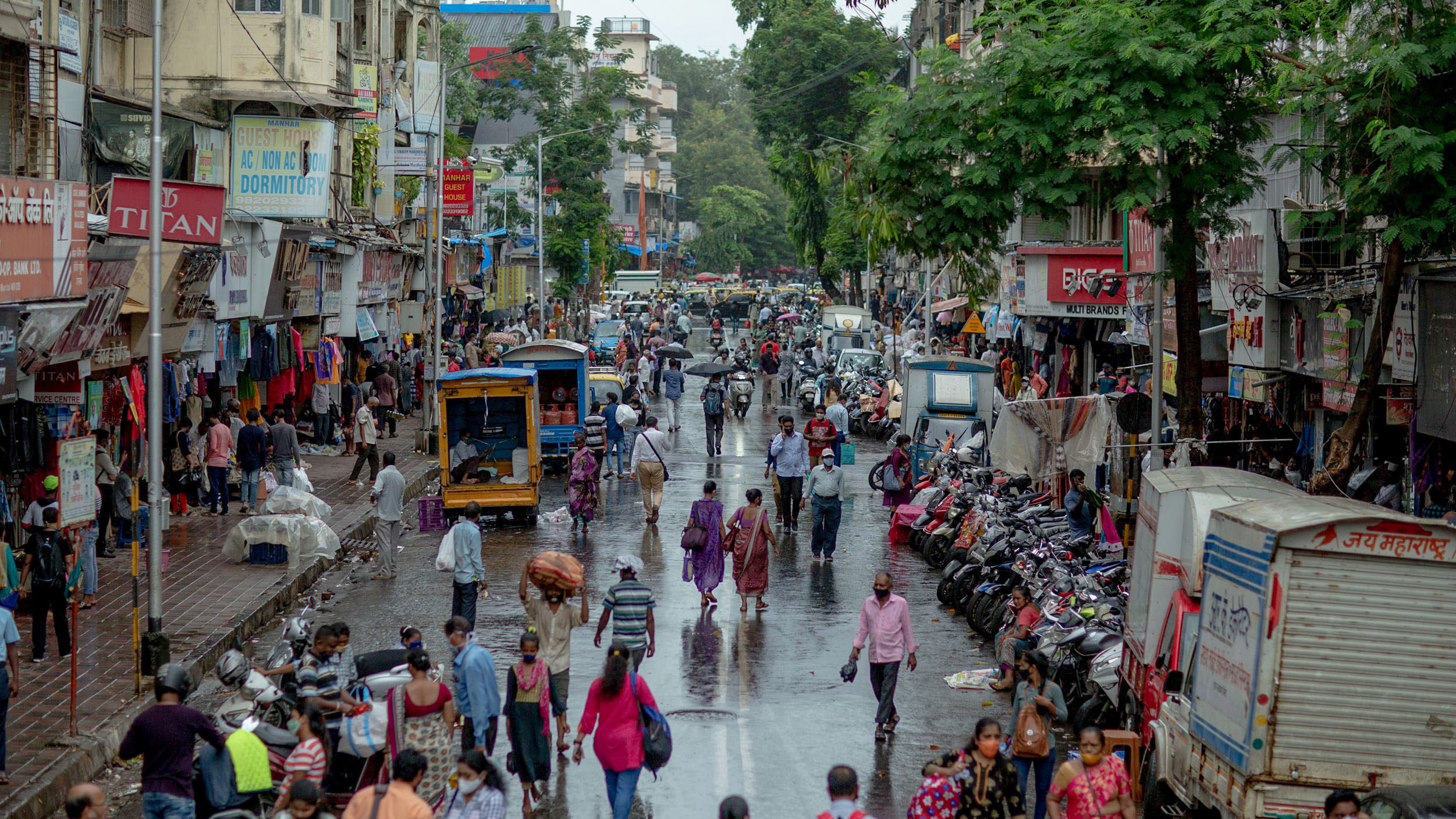 An aerial photograph of a street in Mumbai crowded with pedestrians, delivery trucks and scooters.