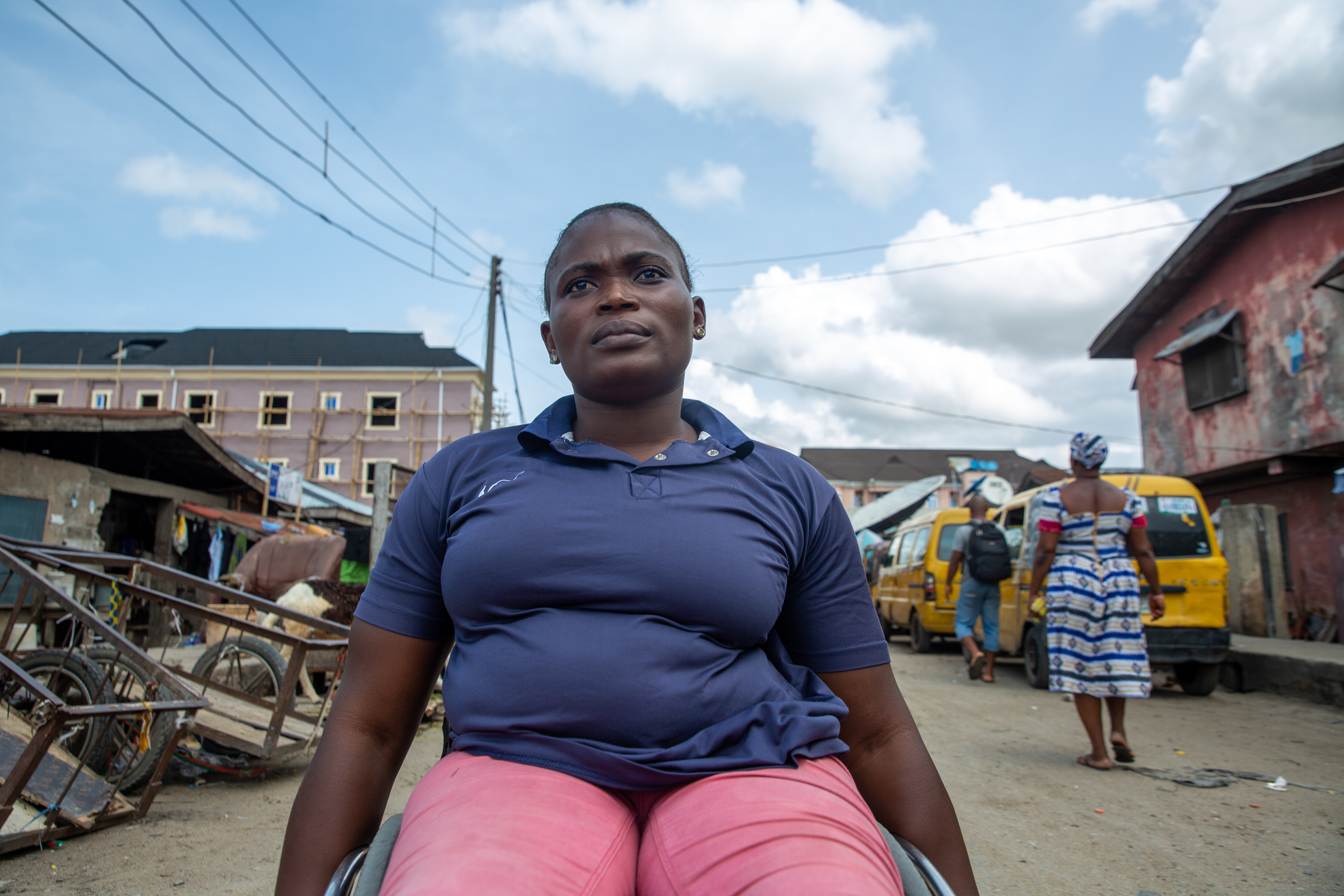 Olajumoke, a 26-year-old woman in a wheelchair, poses for a portrait in the middle of a gravel road in her low-income neighborhood.