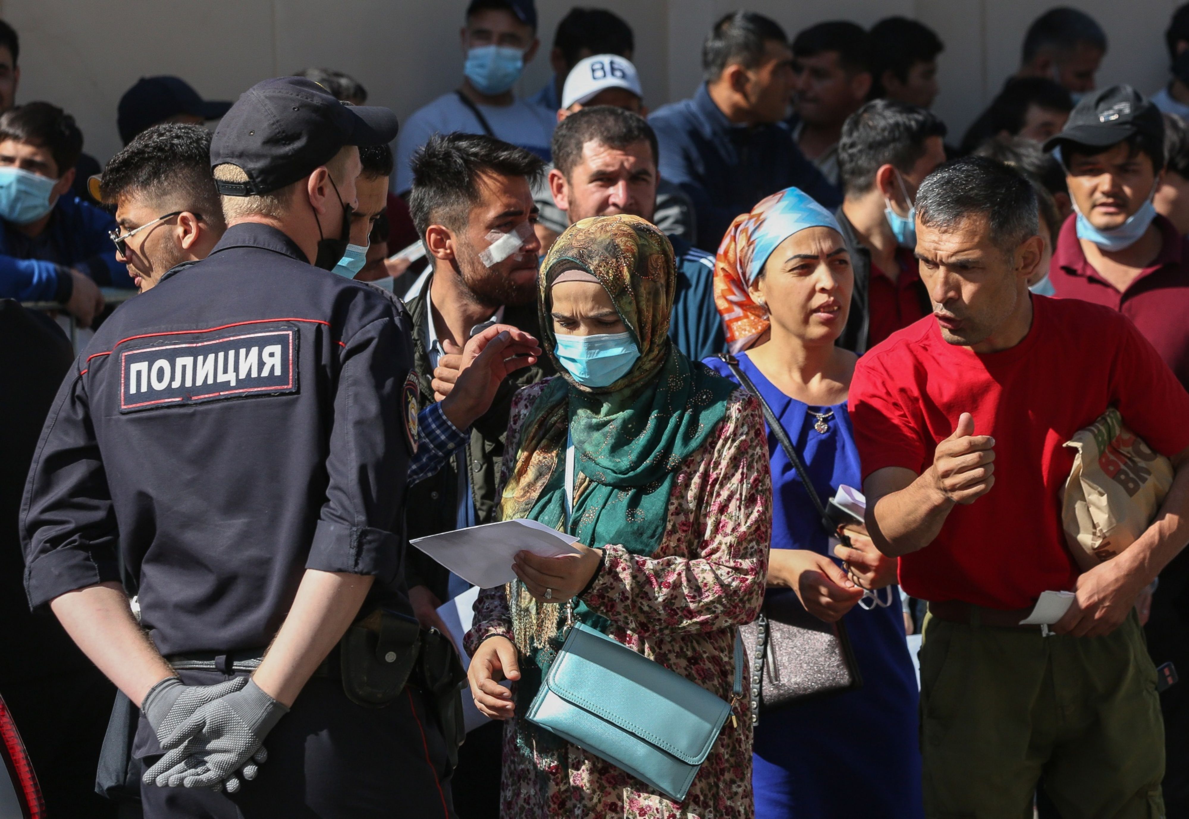 A police officer speaks with a person queuing outside the Tajik embassy office in Moscow, Russia, on Monday, Aug. 10, 2020.