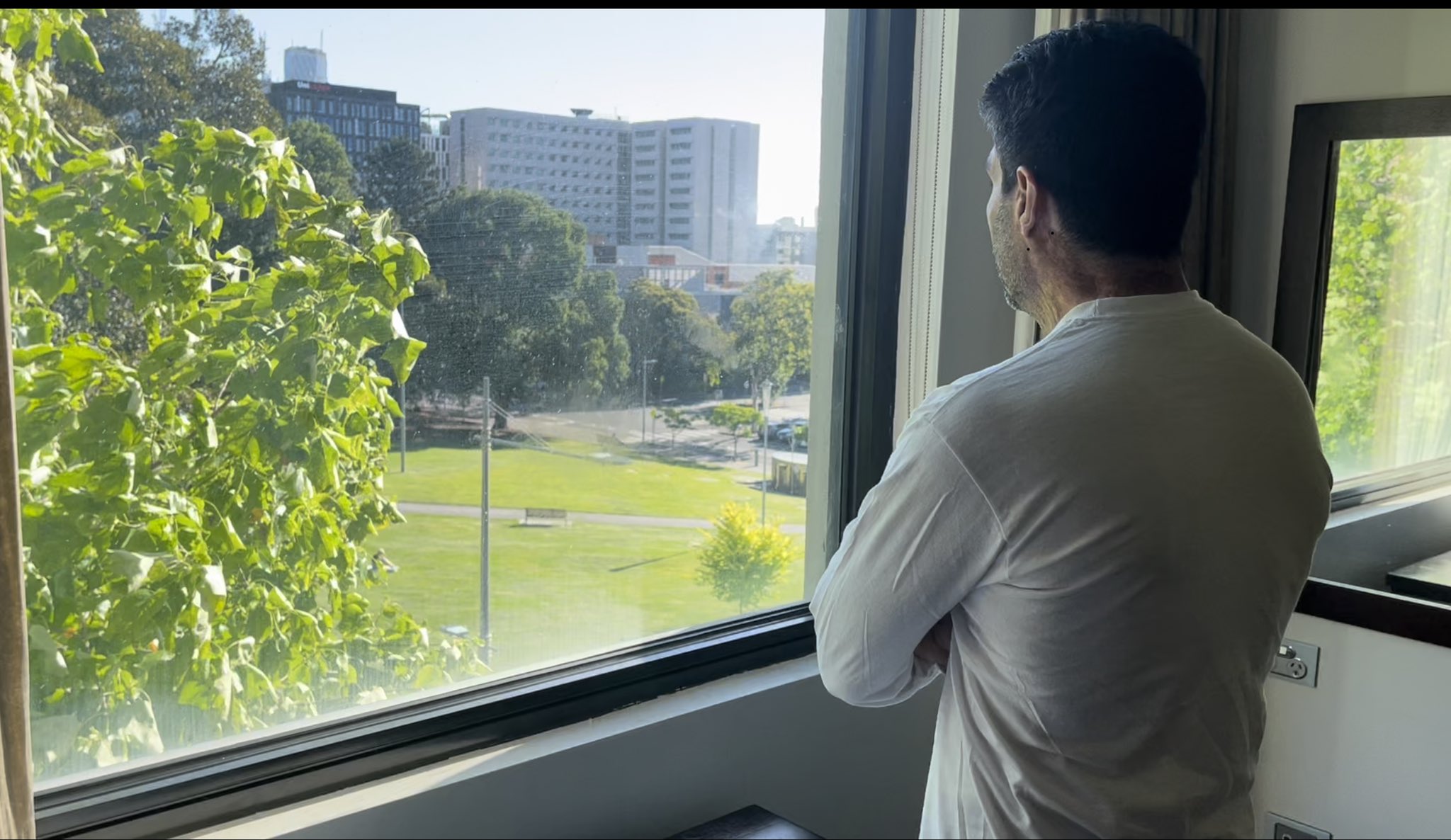 Jamal - in a white shirt with his face obscured - looks out of the window from his room in the Park Hotel to the green expanses of the park and its mature trees