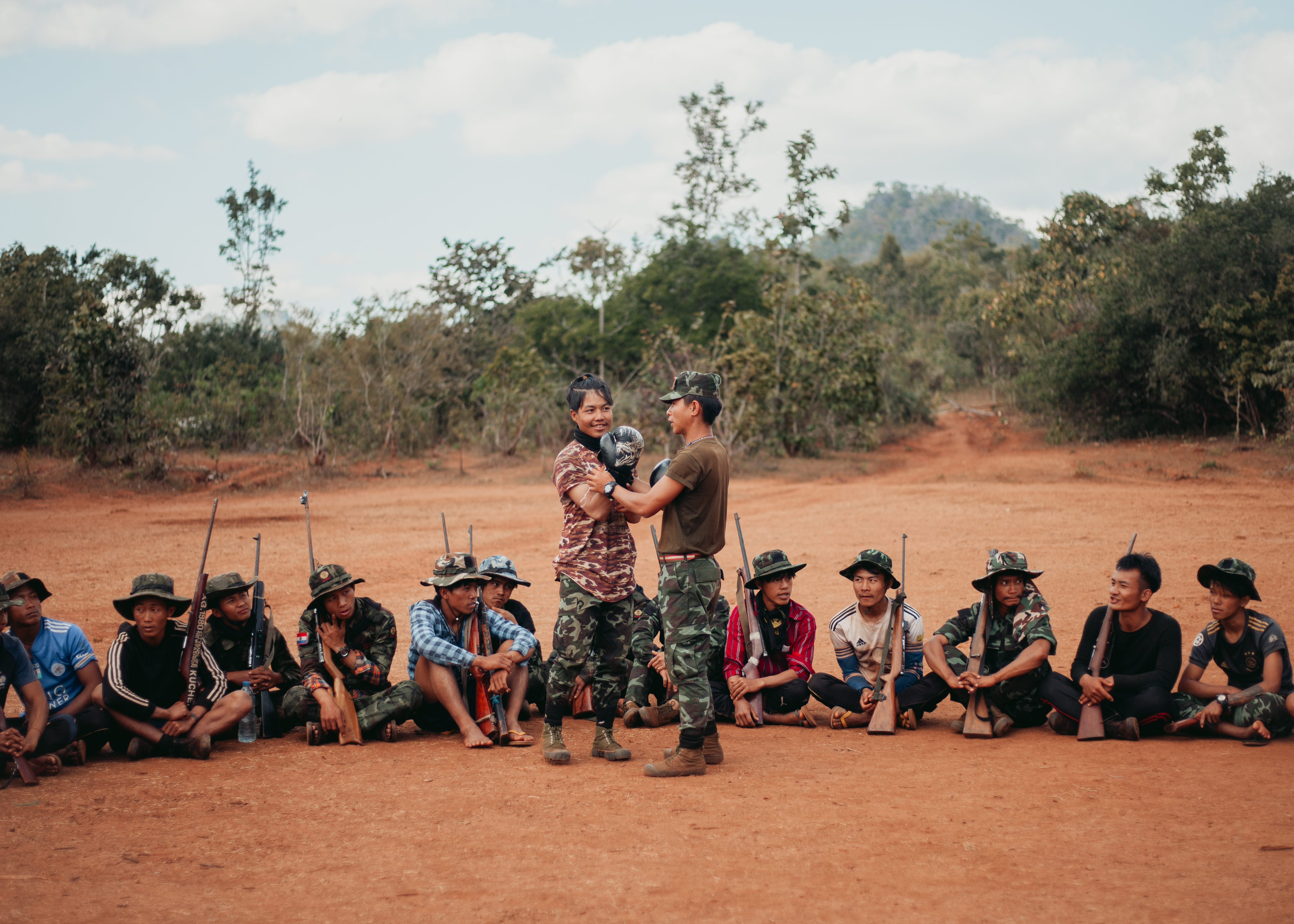 Two cadets train in boxing and hand-to-hand combat, while a group of cadets are seen sitting on the ground, holding their rifles.