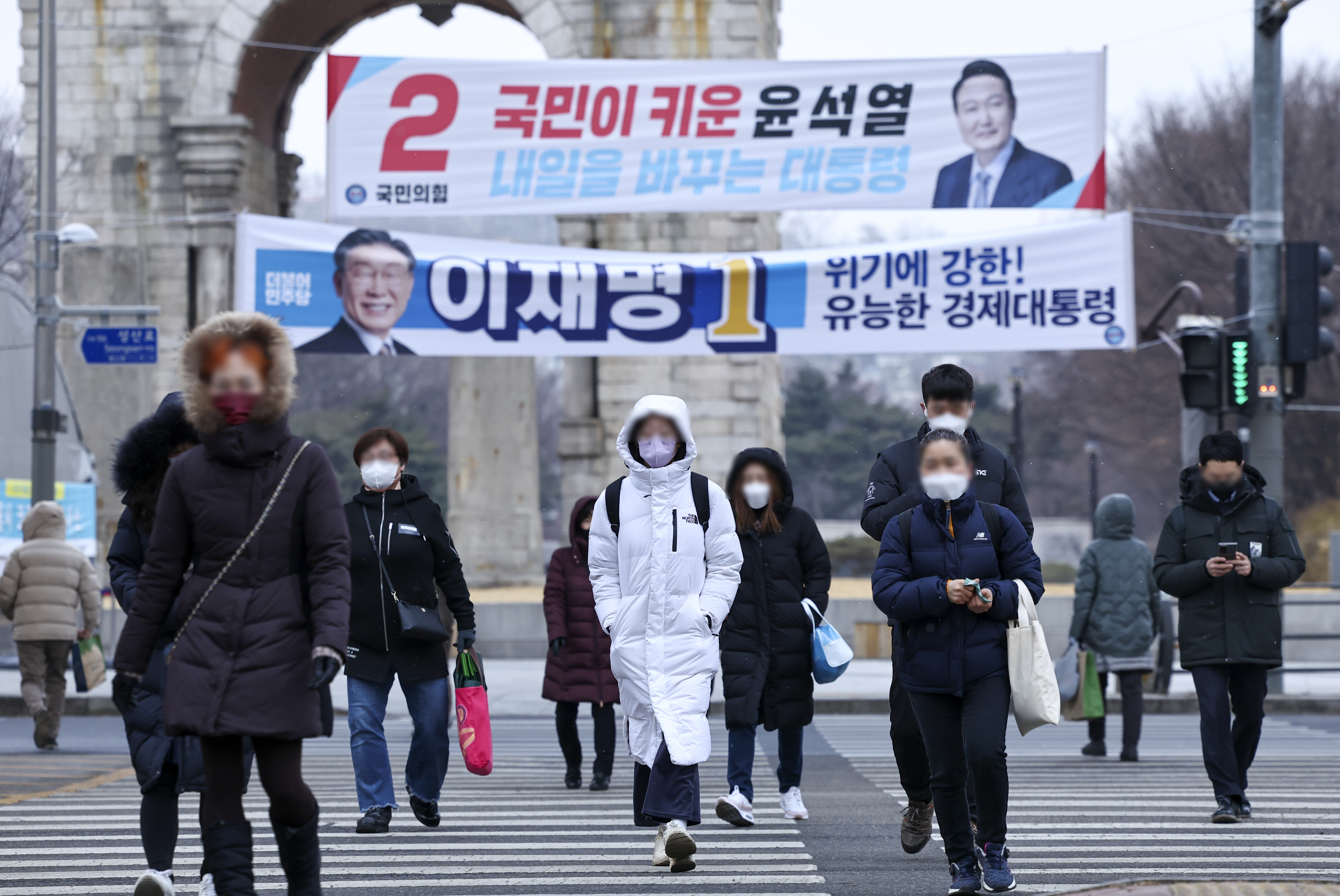People in winter coats cross the street beneath election banners for South Korea's two main election candidates