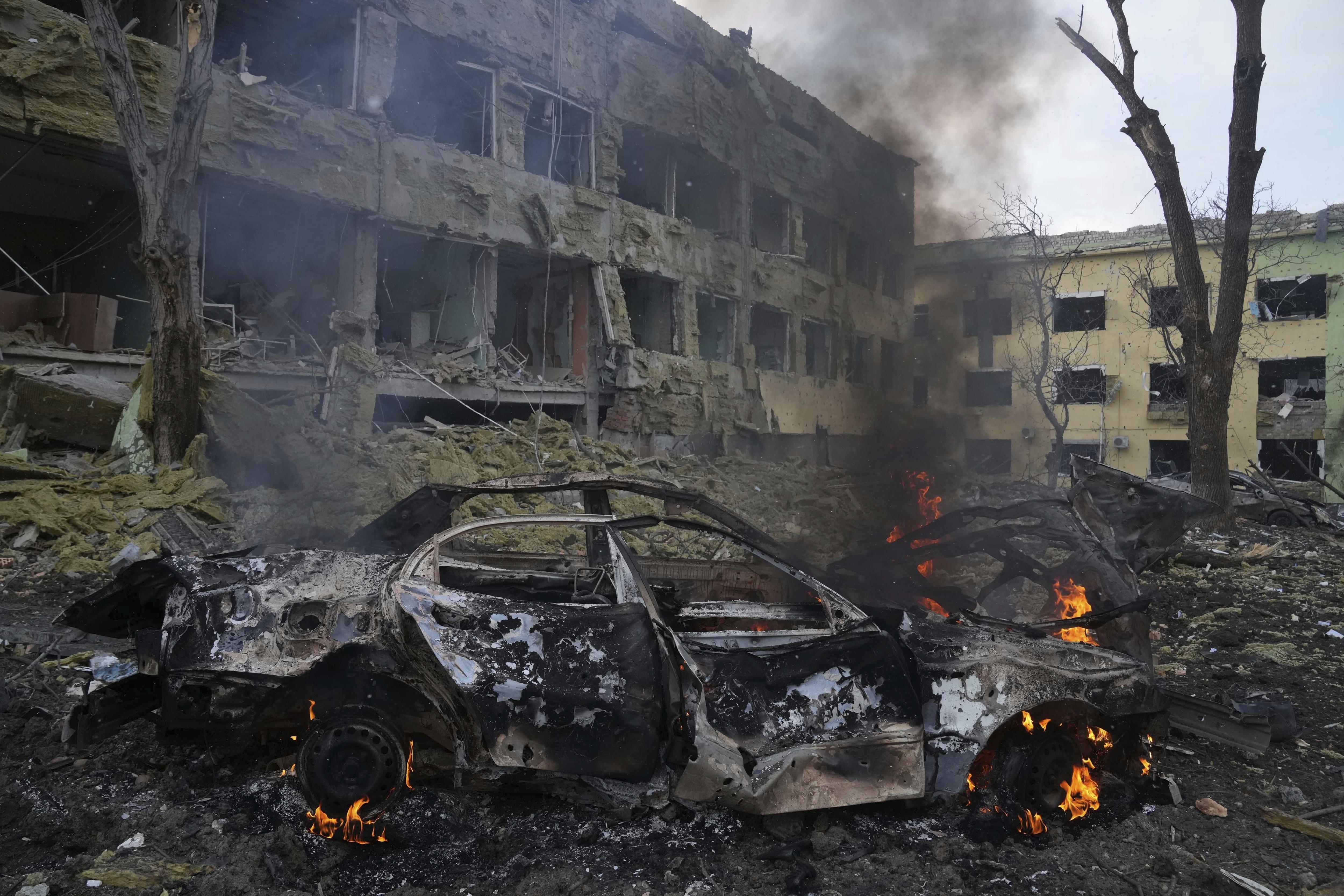 A car burns at the side of the damaged by shelling maternity hospital in Mariupol,