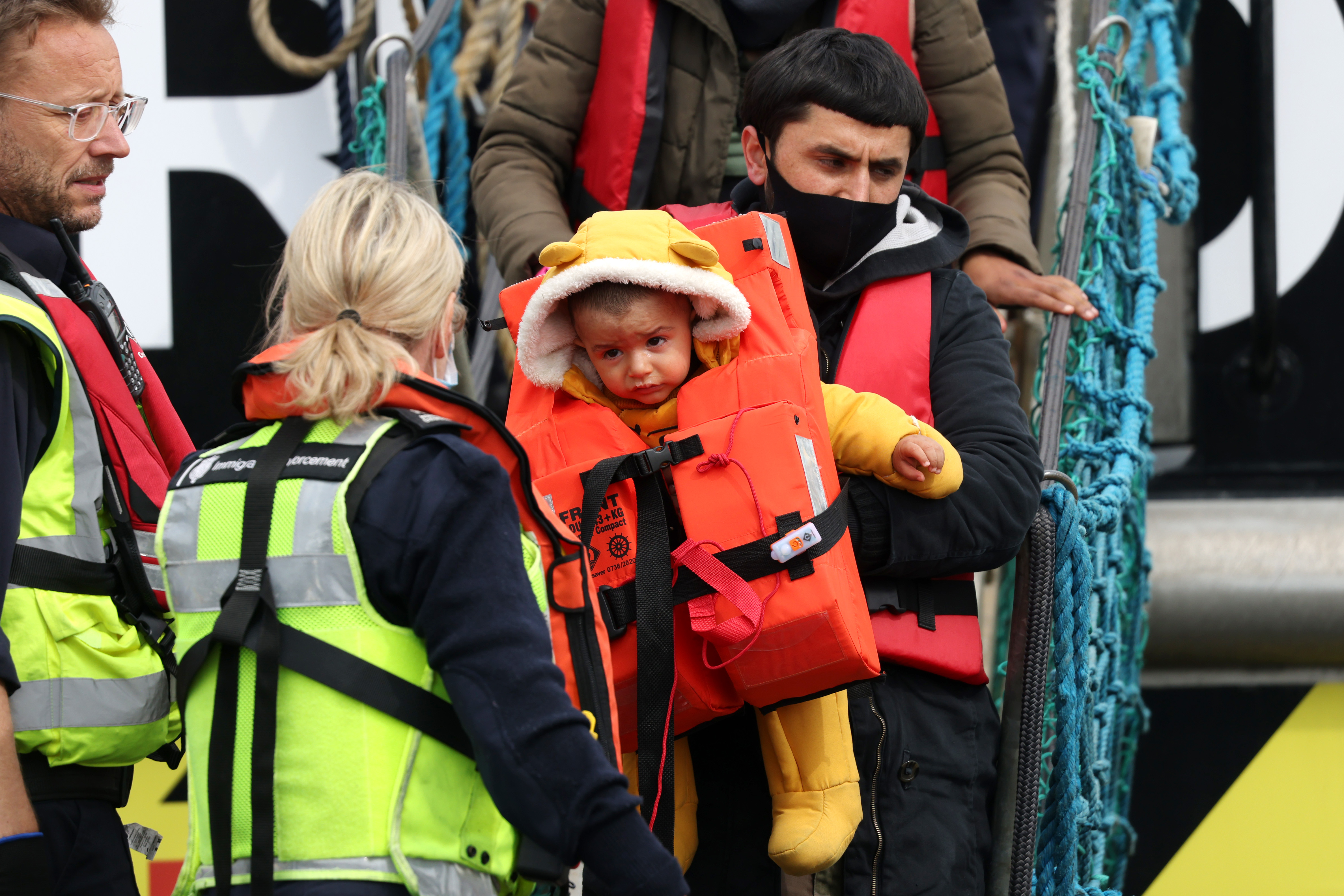 A man carries a child in a life jacket off a boat.