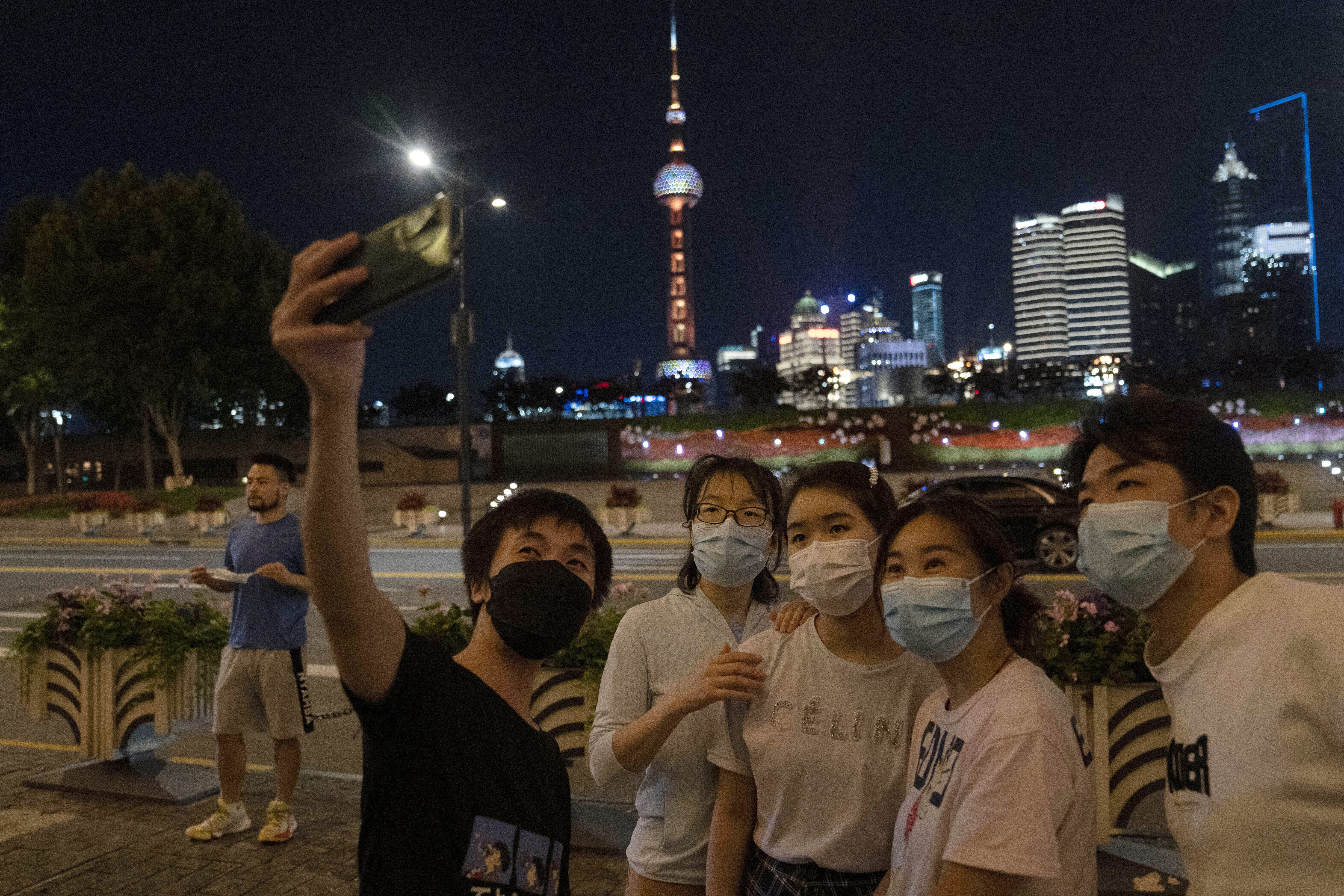A group takes a night time selfie with the Shanghai skyline behind them as lockdown is eased in the city