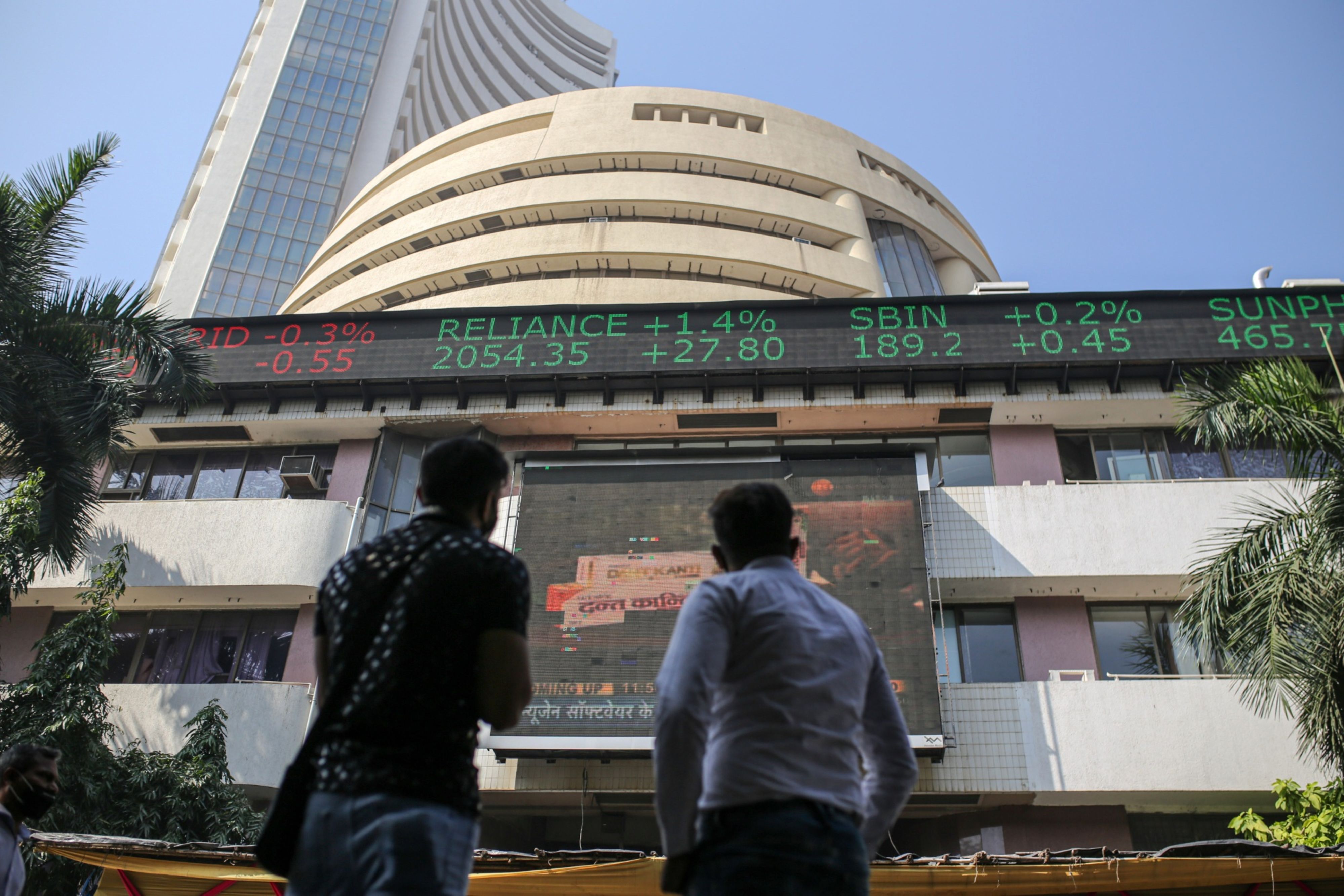People look up at a screen and an electronic ticker board outside the Bombay Stock Exchange (BSE) building in Mumbai, India
