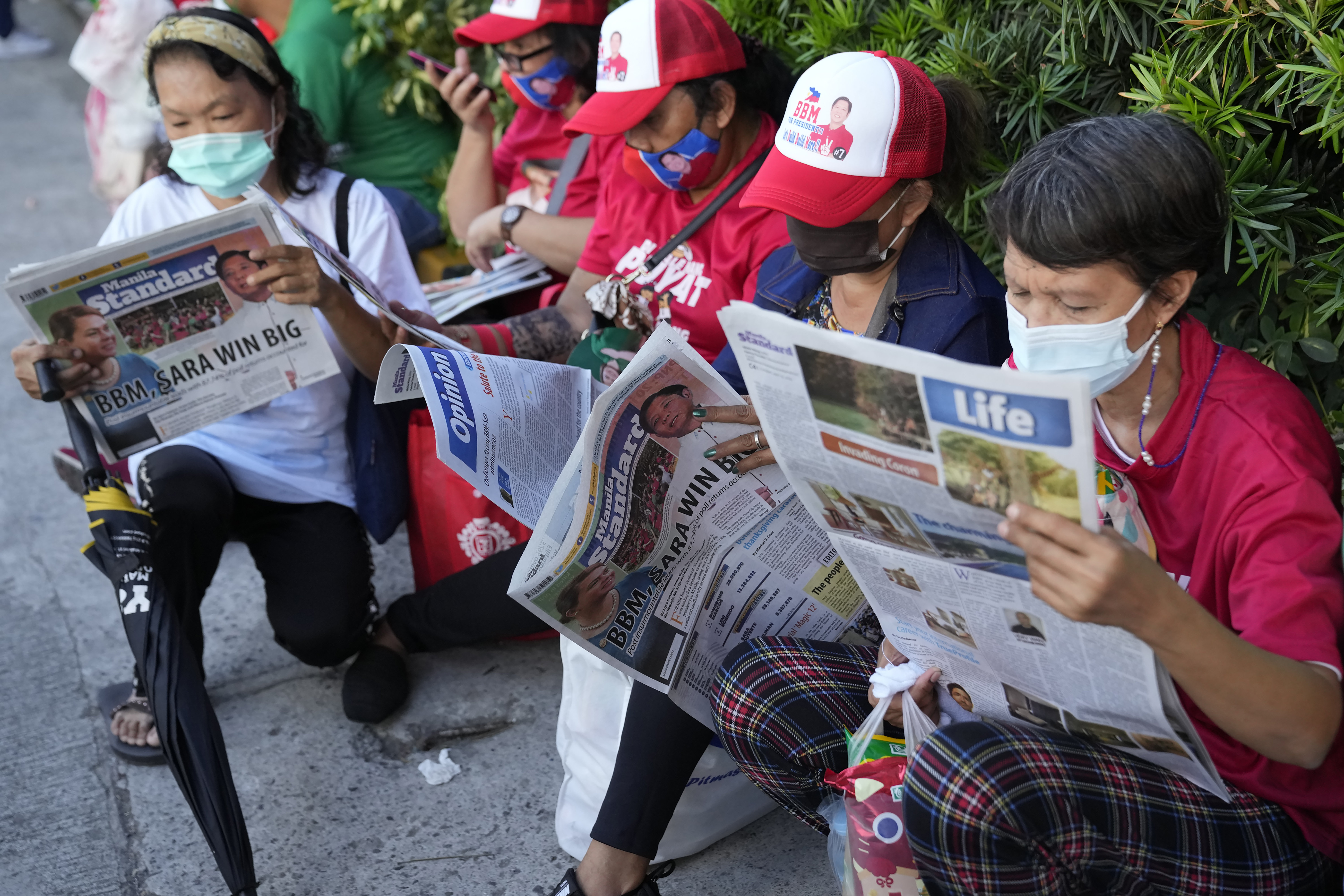 Marcos Jr supporters dressed in red T shirts and baseball caps reading the newspapers reporting his win in the presidential election