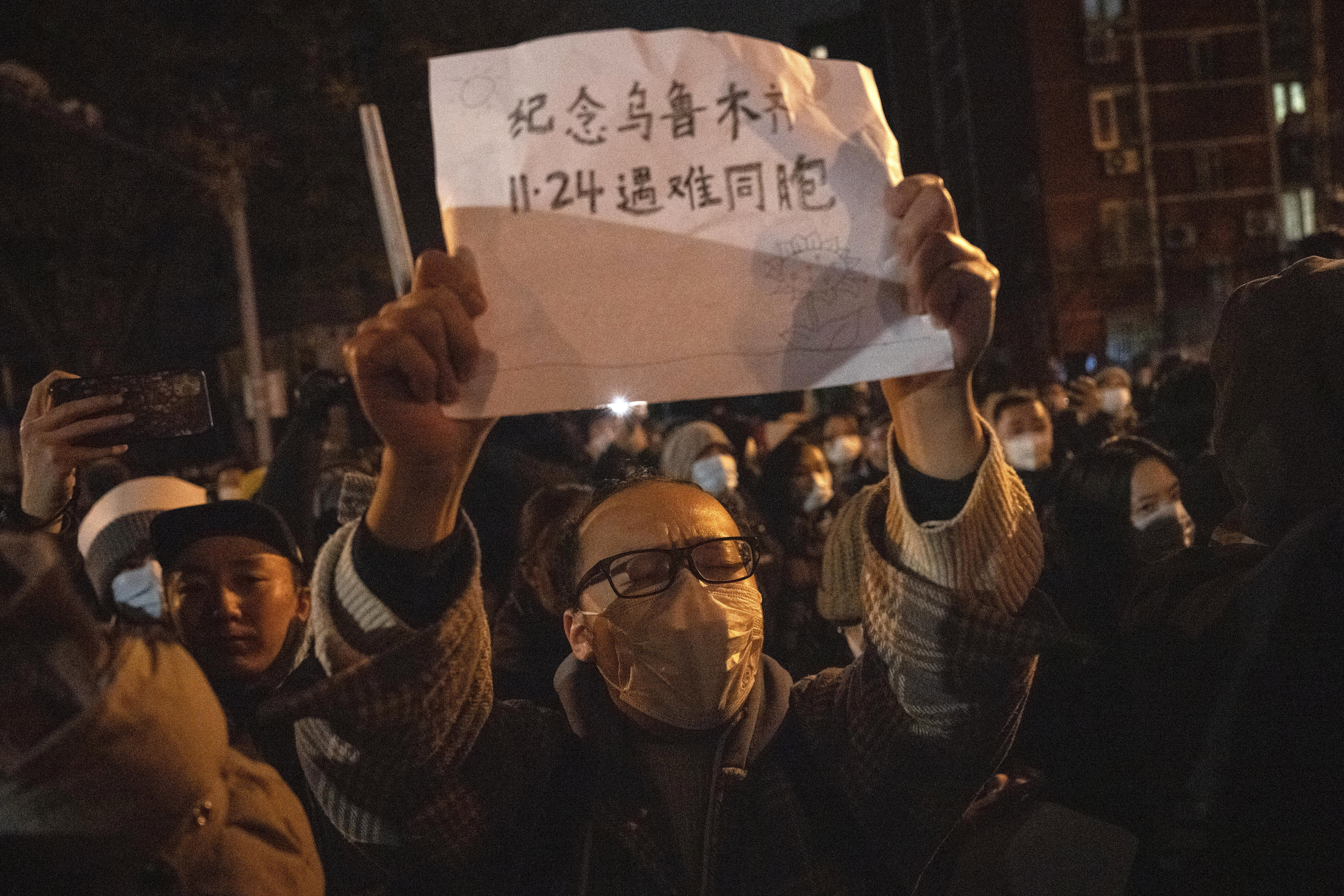A masked protester holds up a sign which reads "Commemorate Urumqi Nov 24 compatriots who died" in Beijing