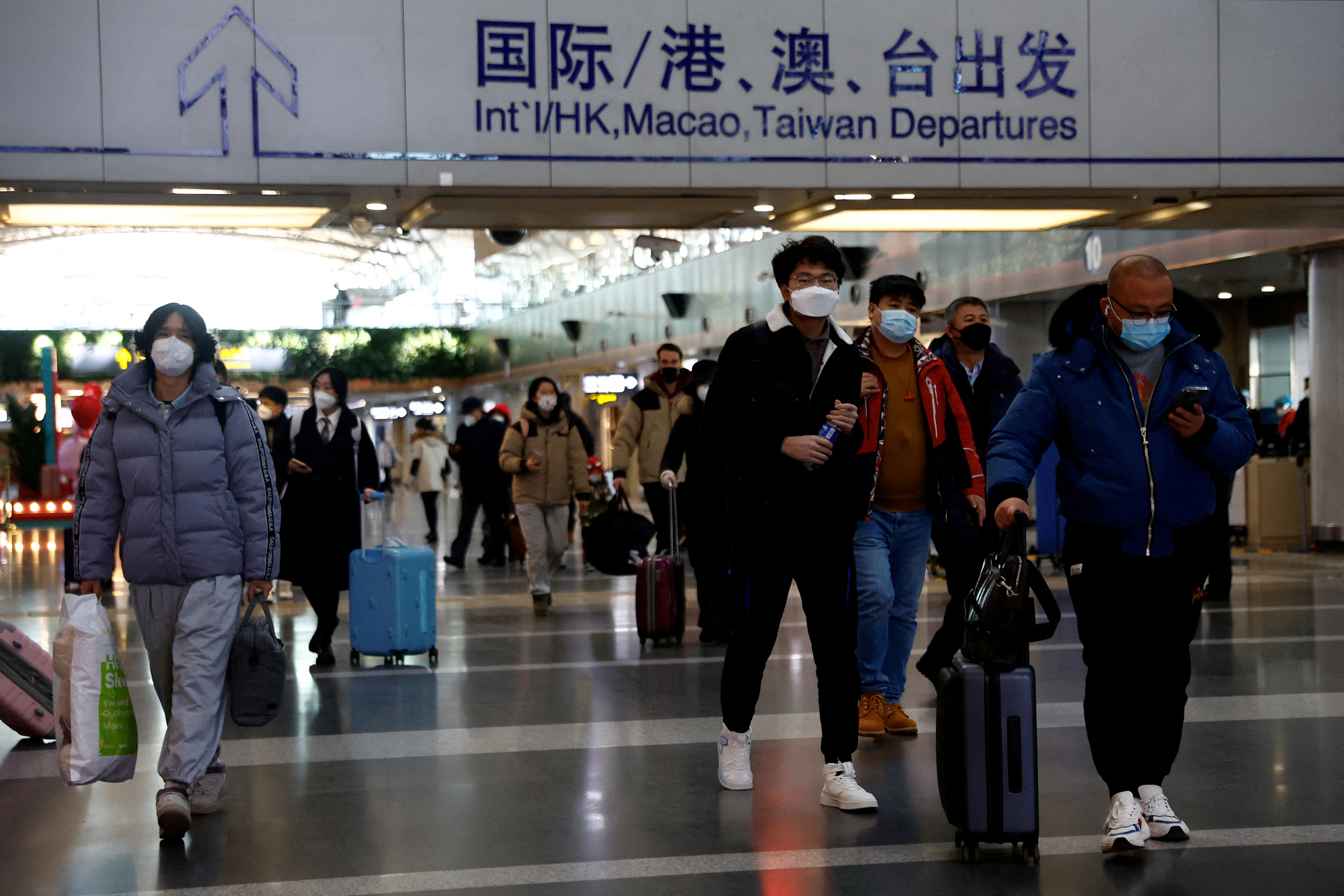 Travellers walk with their luggage at Beijing Capital International Airport
