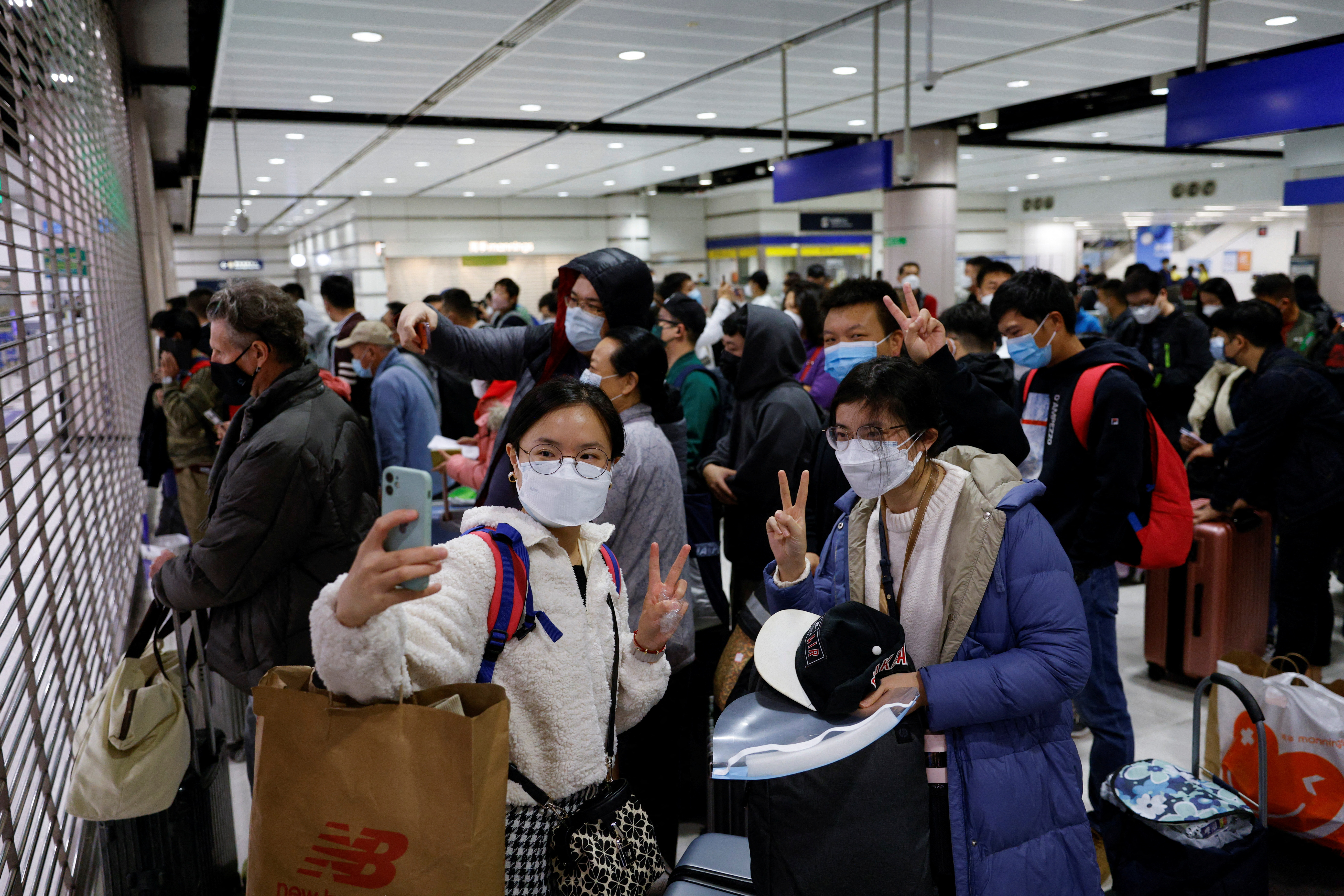 Women take selfies as they wait for the Hong Kong-China border crossing to reopen. They are indoors, at the Lok Ma Chau crossing. The metal shutter is pulled down. They look excited and are making V signs with their fingers